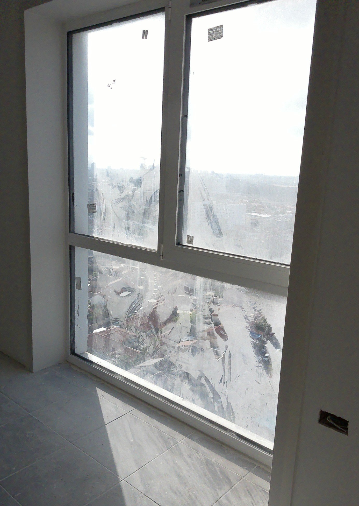 Large window with construction debris view, sunlight casting shadows on tiled floor, partially open for ventilation.