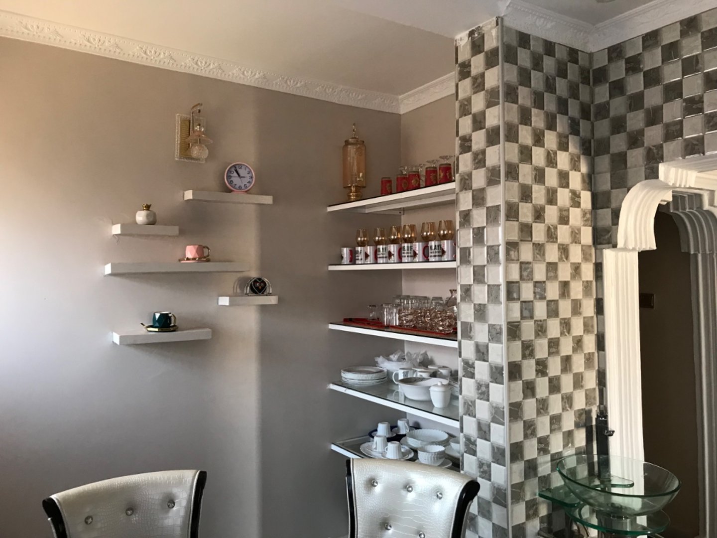 Modern kitchen corner with floating shelves, decorative items, plates, cups, and a checkered wall design.