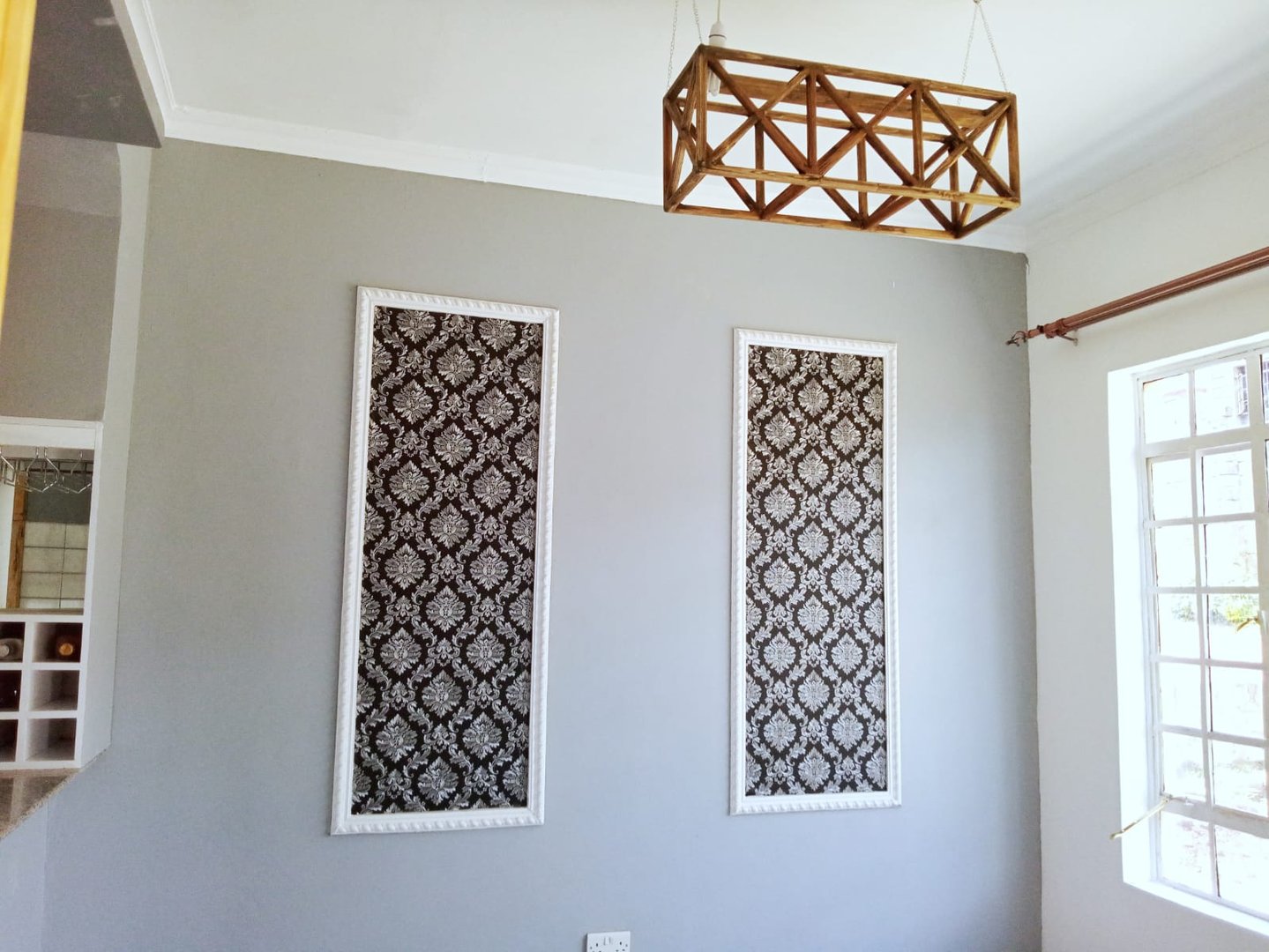Two decorative panels with black and white patterns on a gray wall, below a geometric wooden light fixture.