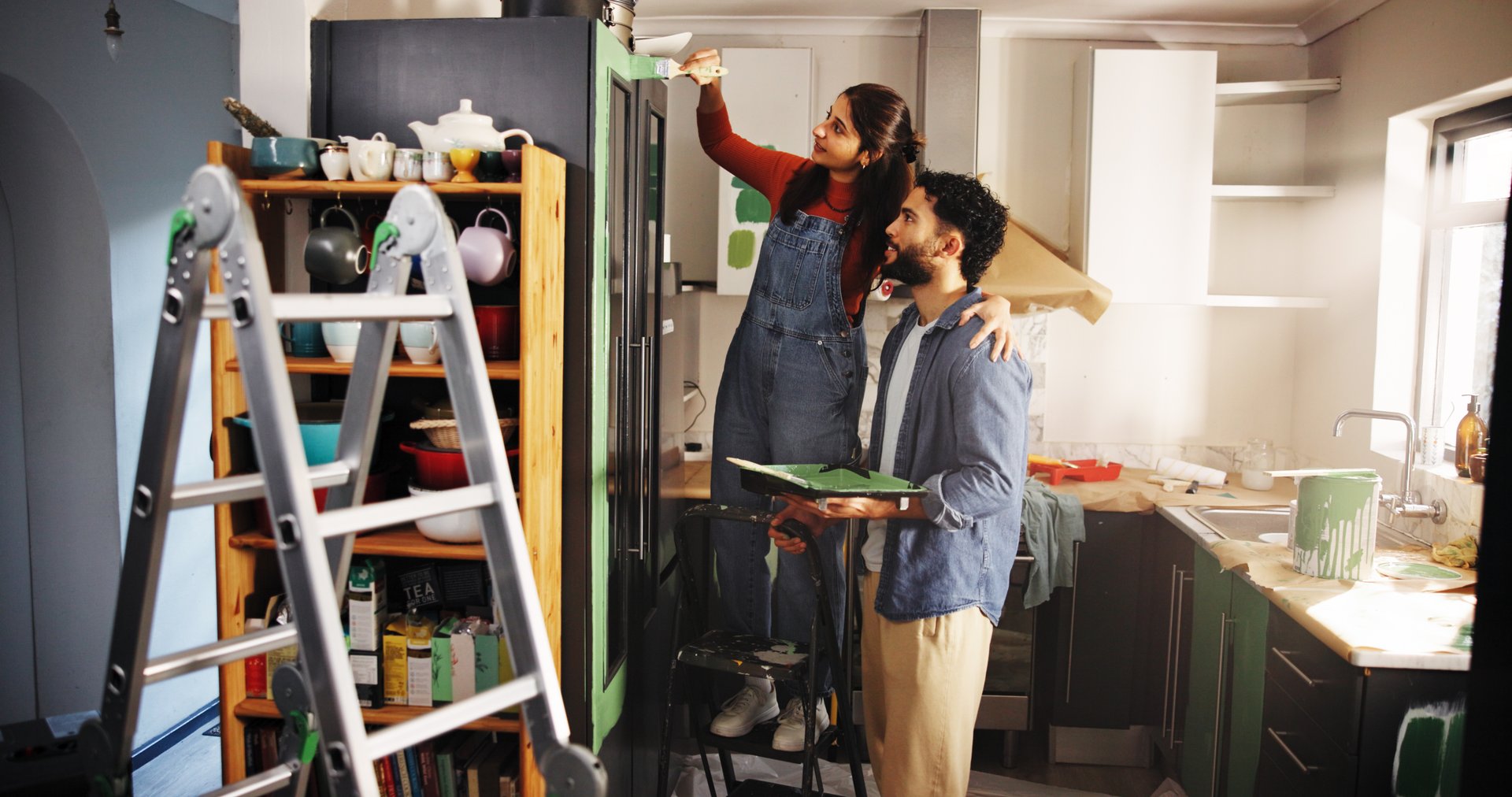 Couple, help and painting kitchen at new house for renovation, interior design and decoration. People, support and furniture with paint brush for diy improvement, remodeling and repairs maintenance