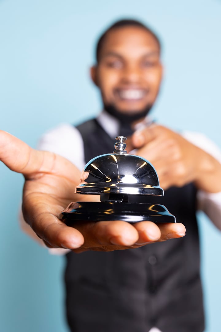 Bellhop doorkeeper ringing the service bell to present his help and assistance upon the guests arrival against blue background. Hotel porter providing great luxury services at resort.