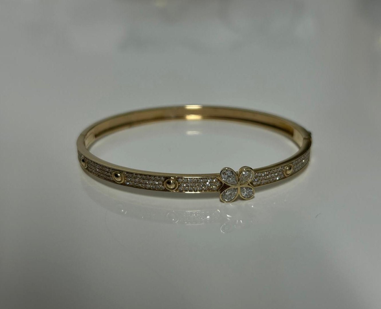 Gold bracelet with diamond accents and a central butterfly design on a reflective surface.