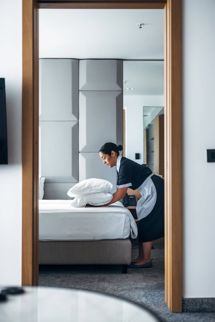 A housekeeper preparing a hotel bed by arranging pillows, creating a clean and welcoming space.