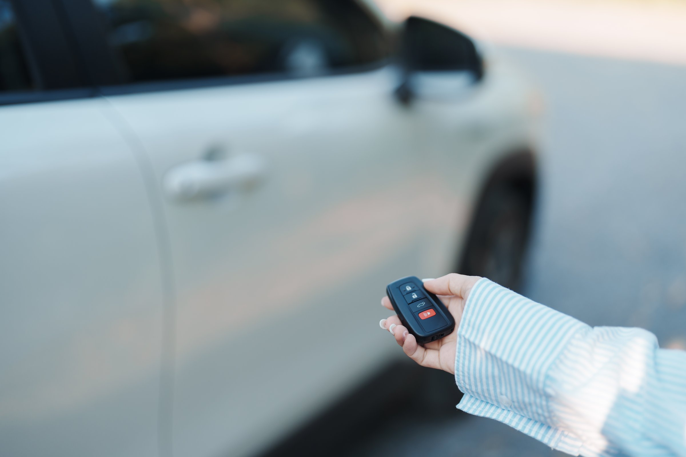 Hand holding car remote control, smart key to lock or unlock doors of white car. Safety, travel and transportation concept