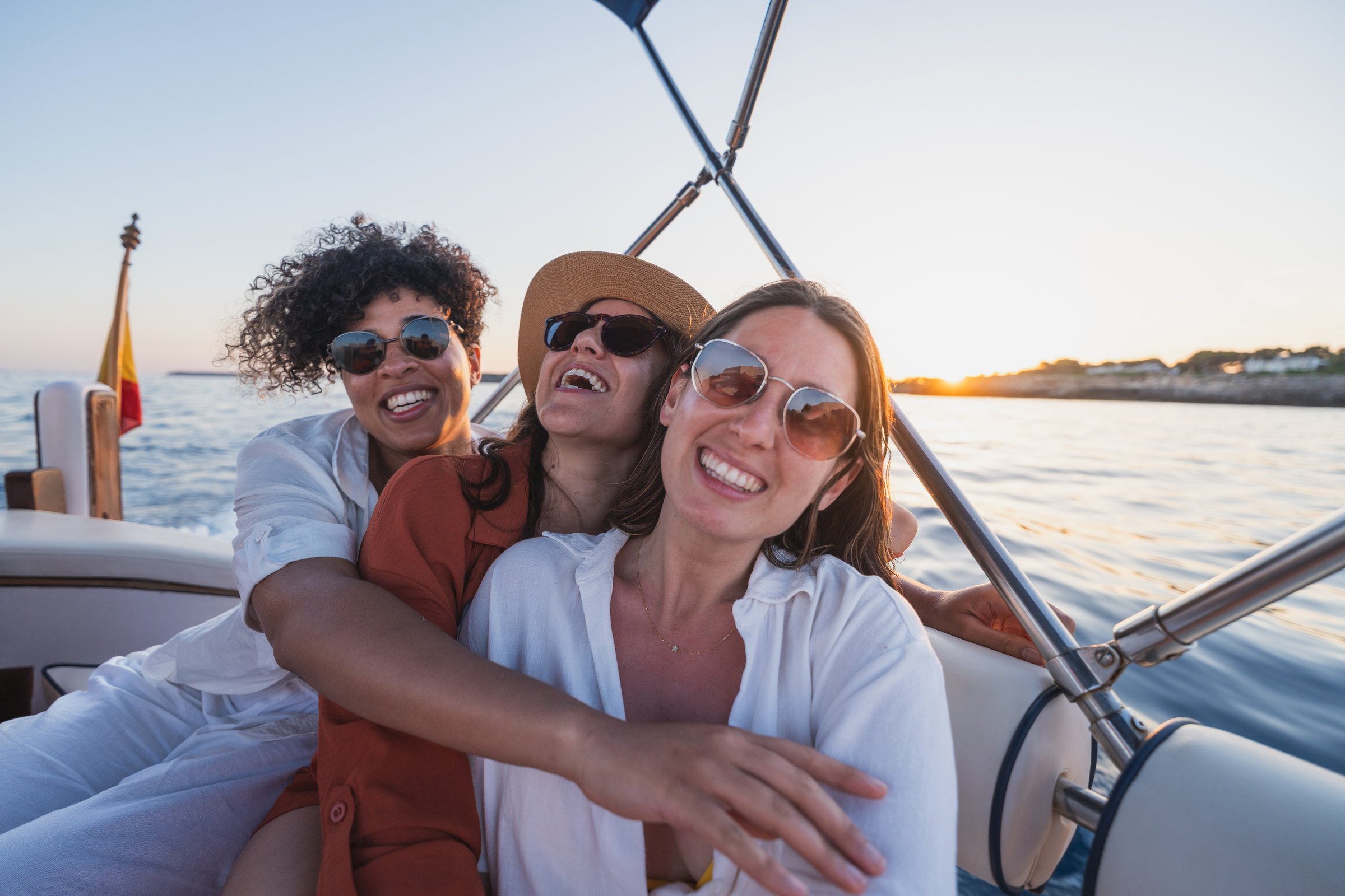 Female friends embracing and smiling while sailing at golden hour. Summer, vacation, boat concept