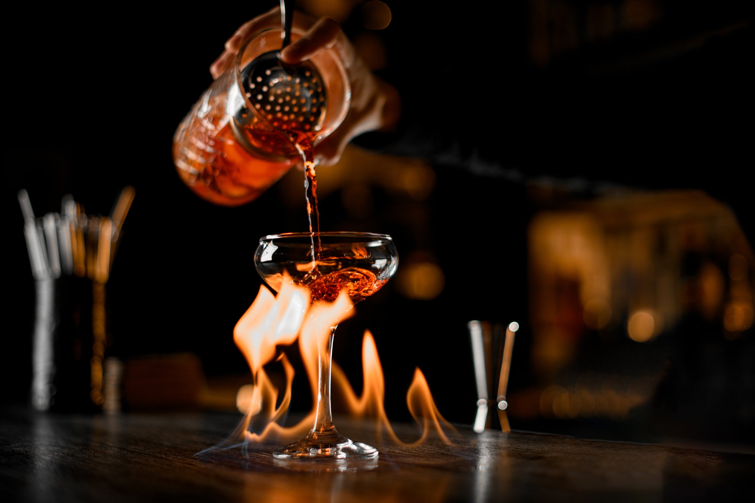 Cocktail maker master make a luxurious alcohol strong drinks with fire on a blurred dark background