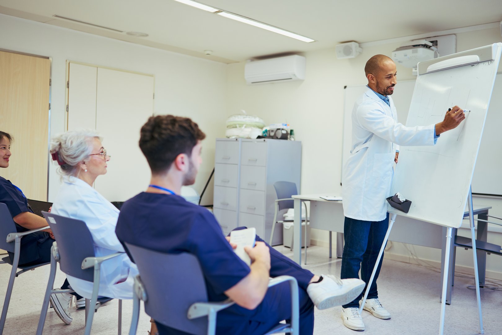 Doctor giving a presentation to his medical team in a hospital conference room, writing on a whiteboard