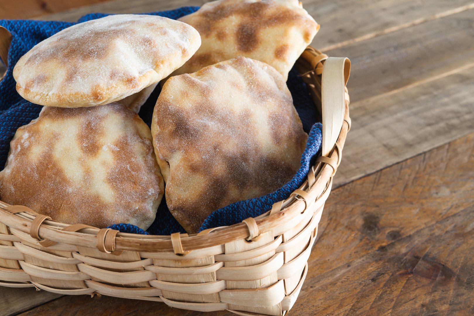 Wooden basket with several pieces of homemade pita bread on wooden table. Copy space.