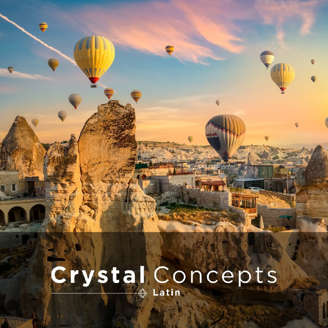 Hot air balloons float over rocky formations at sunrise, with a Crystal Concepts Latin logo overlay on the photo.