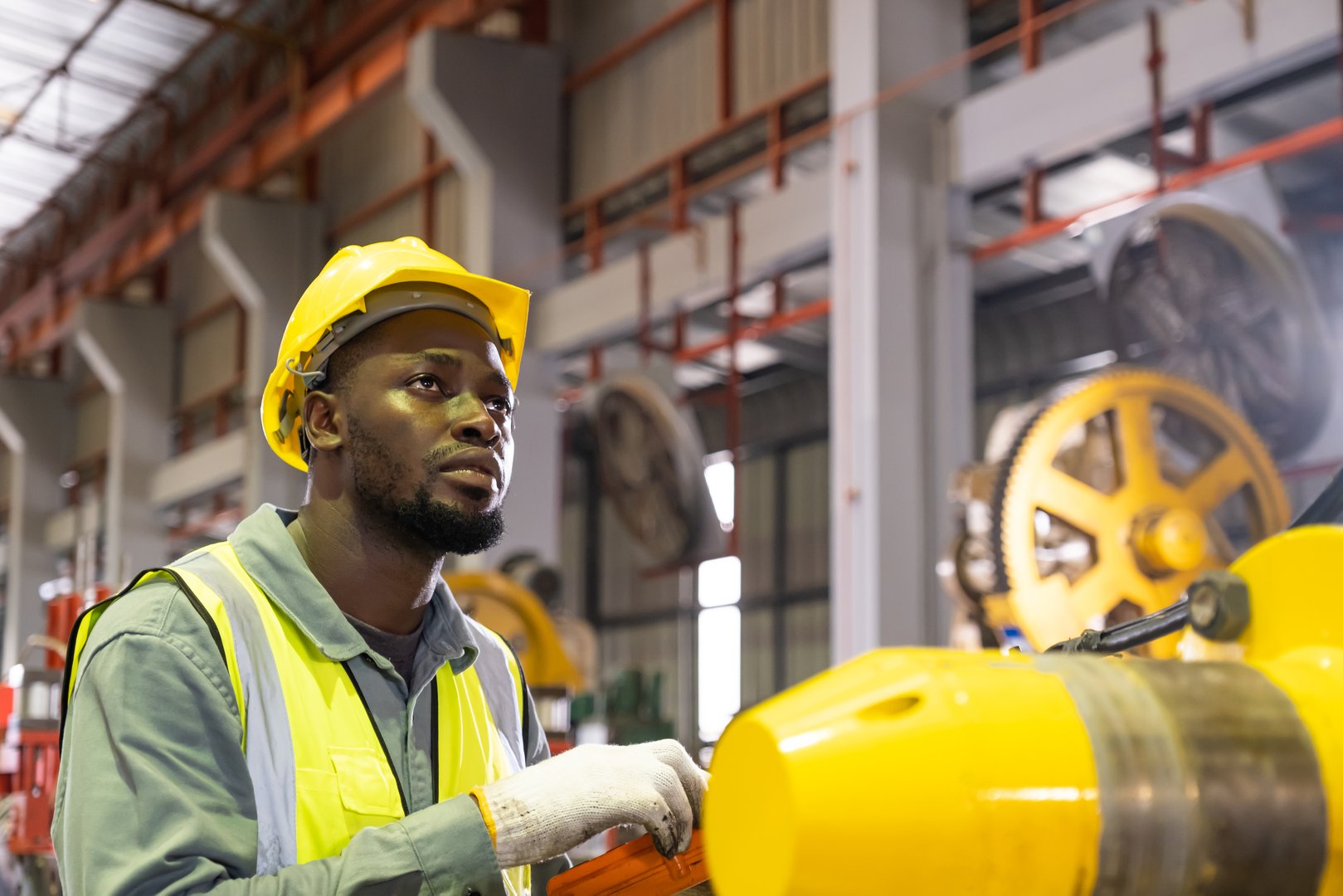 African men mechanical engineer, wearing safety equipment. While operate machine on production line and safety control while work inside of factory area. With blurred background of heavy machine.