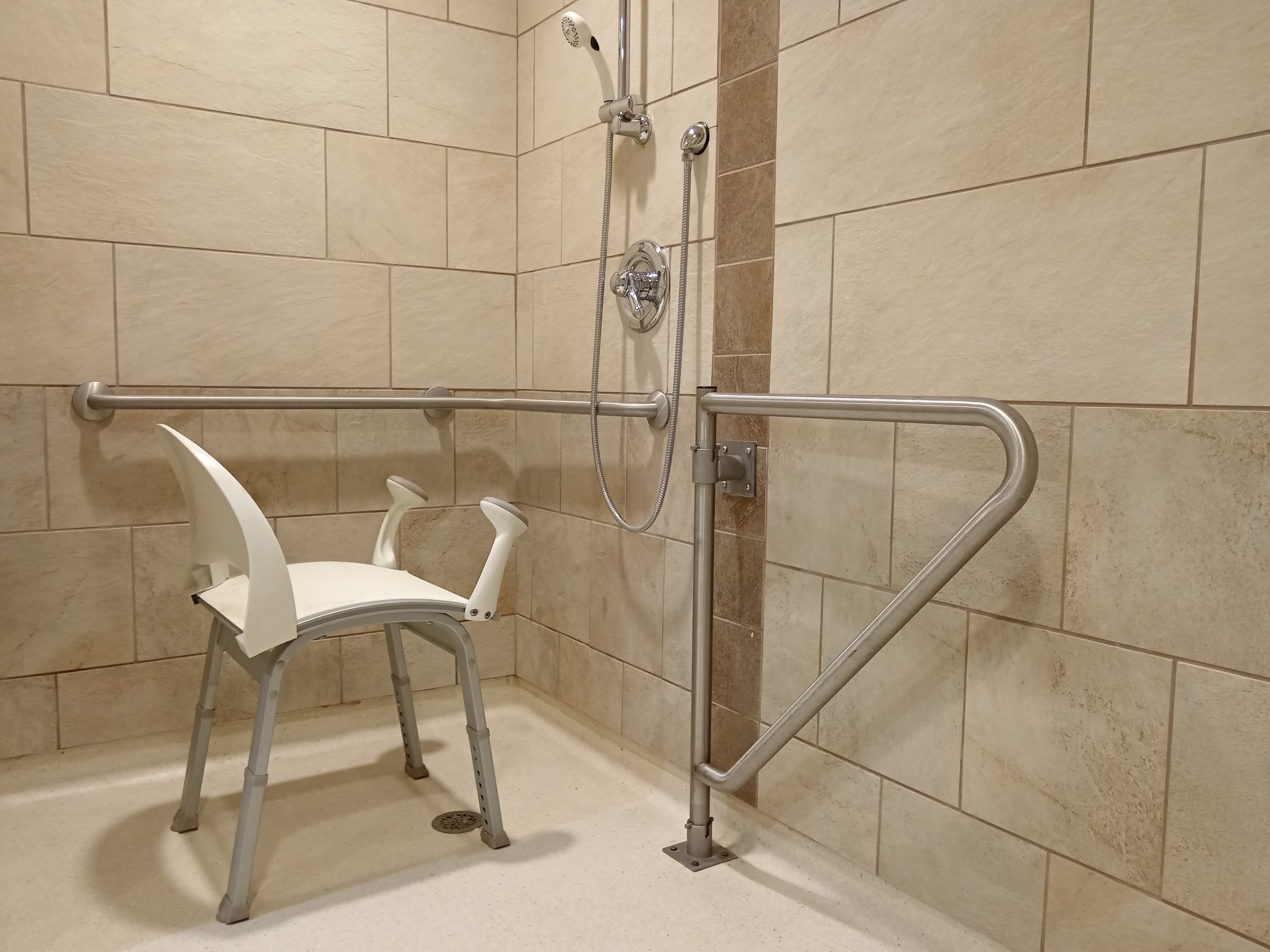 Medical shower chair with grab bars for seniors and disability person in bathroom care home facility.