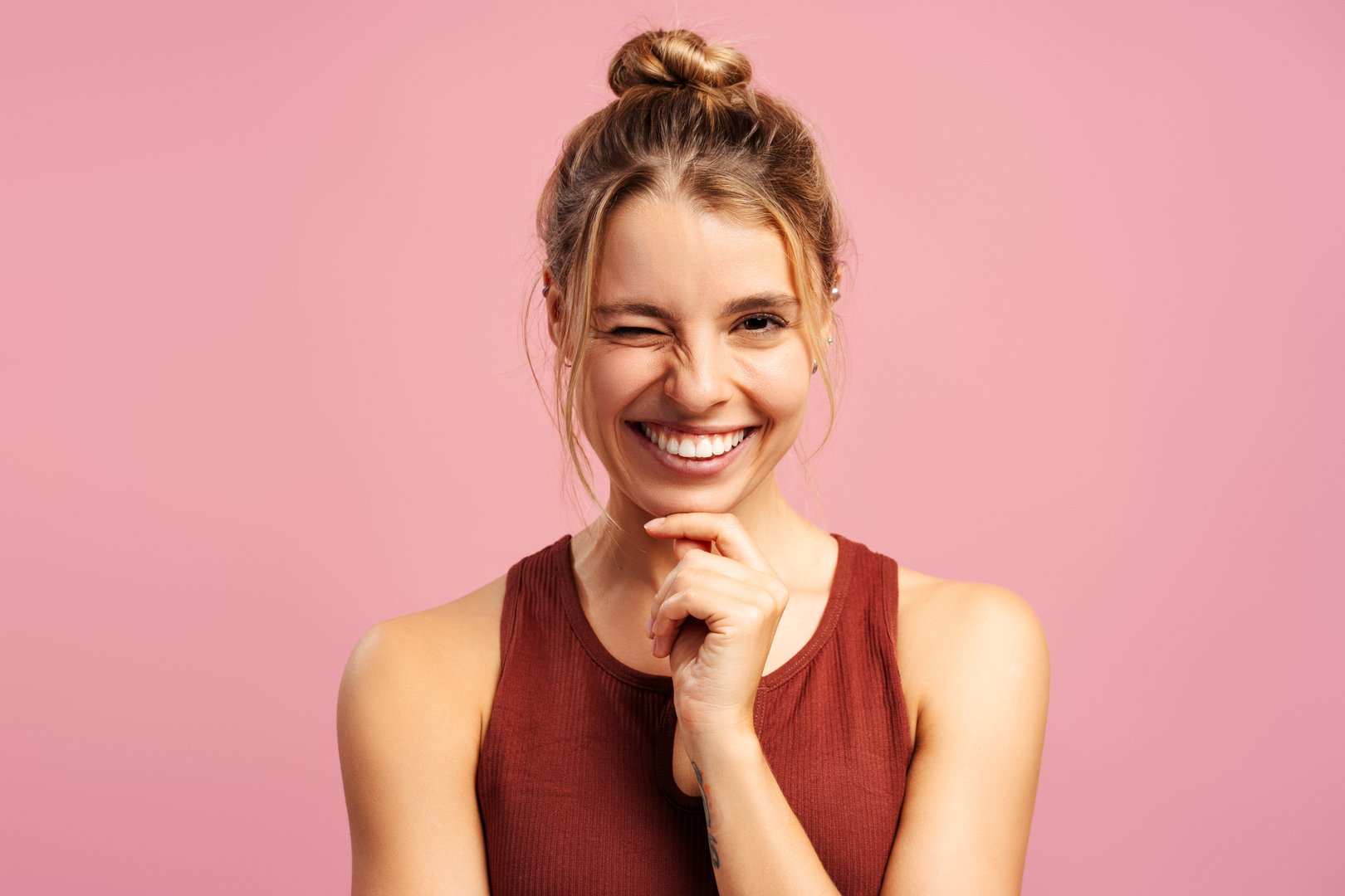 Happy fit beautiful young woman in sportwear holding hand on cheek, winking, looking at camera in studio. Sport, health care, wellness concept