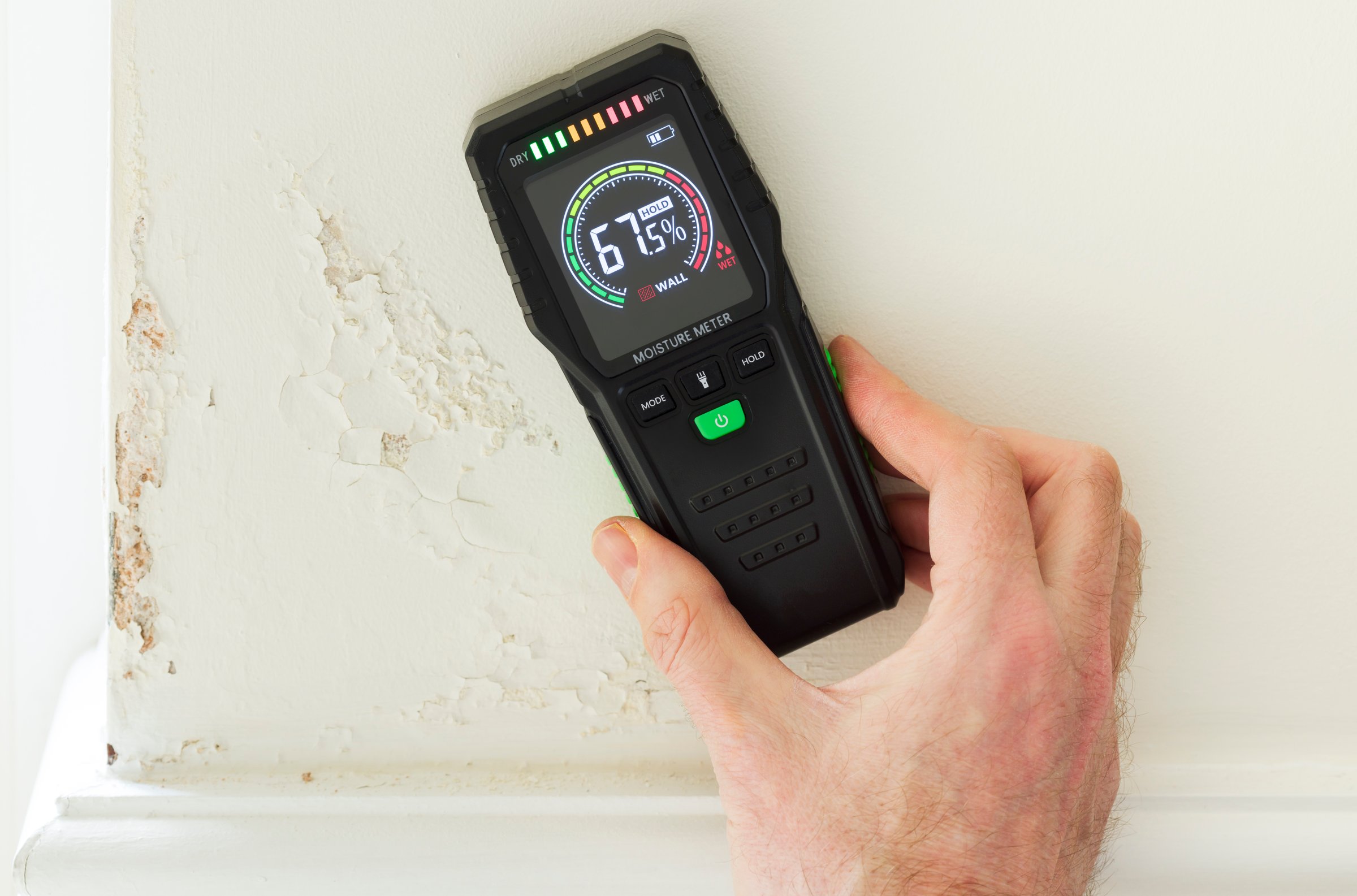 Moisture detector (moisture testing meter) against a wall with rising damp, reading high moisture content. UK home interior