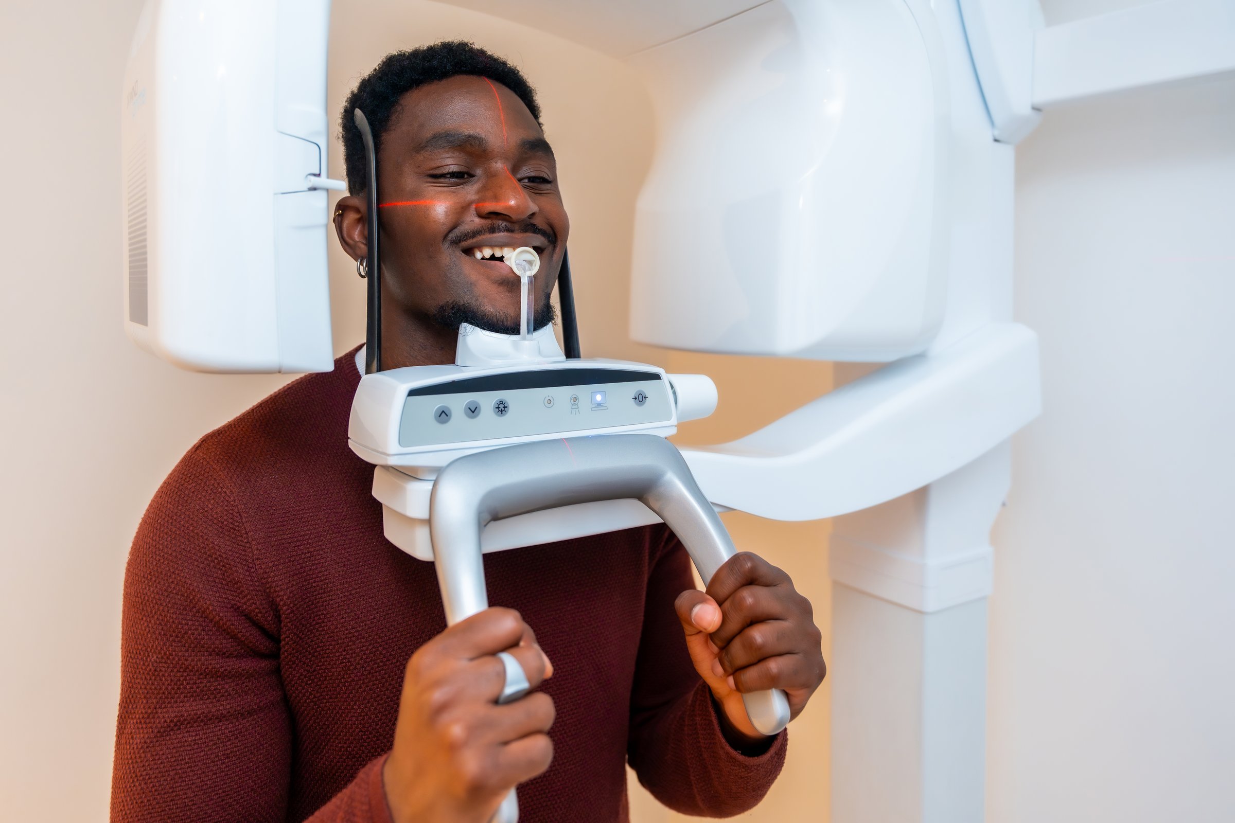 Young adult man smiling while undergoing a dental x-ray scan in a modern dental clinic, showcasing advanced dental technology