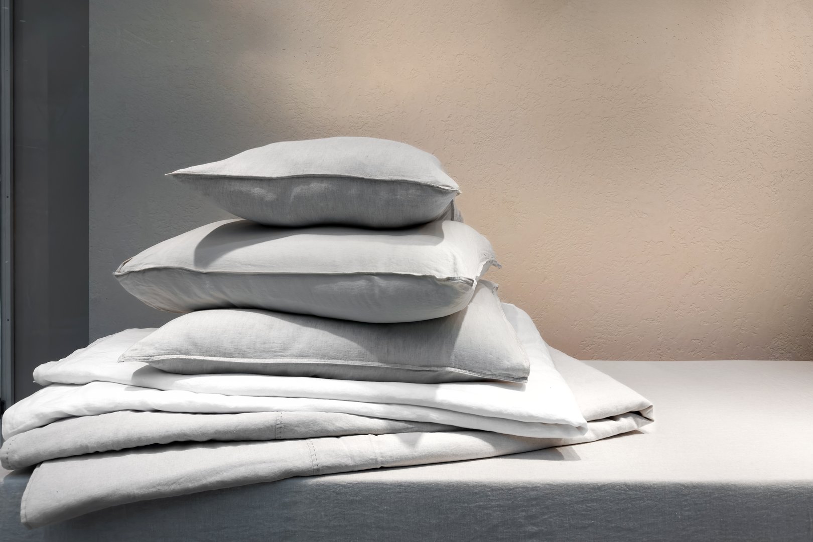 Housekeeping, laundry day concept. Clean bedding, memory foam pillows in french pillowcases and down blanket on mattress in bedroom. Textile on bed, blanket and cushions against copy space background