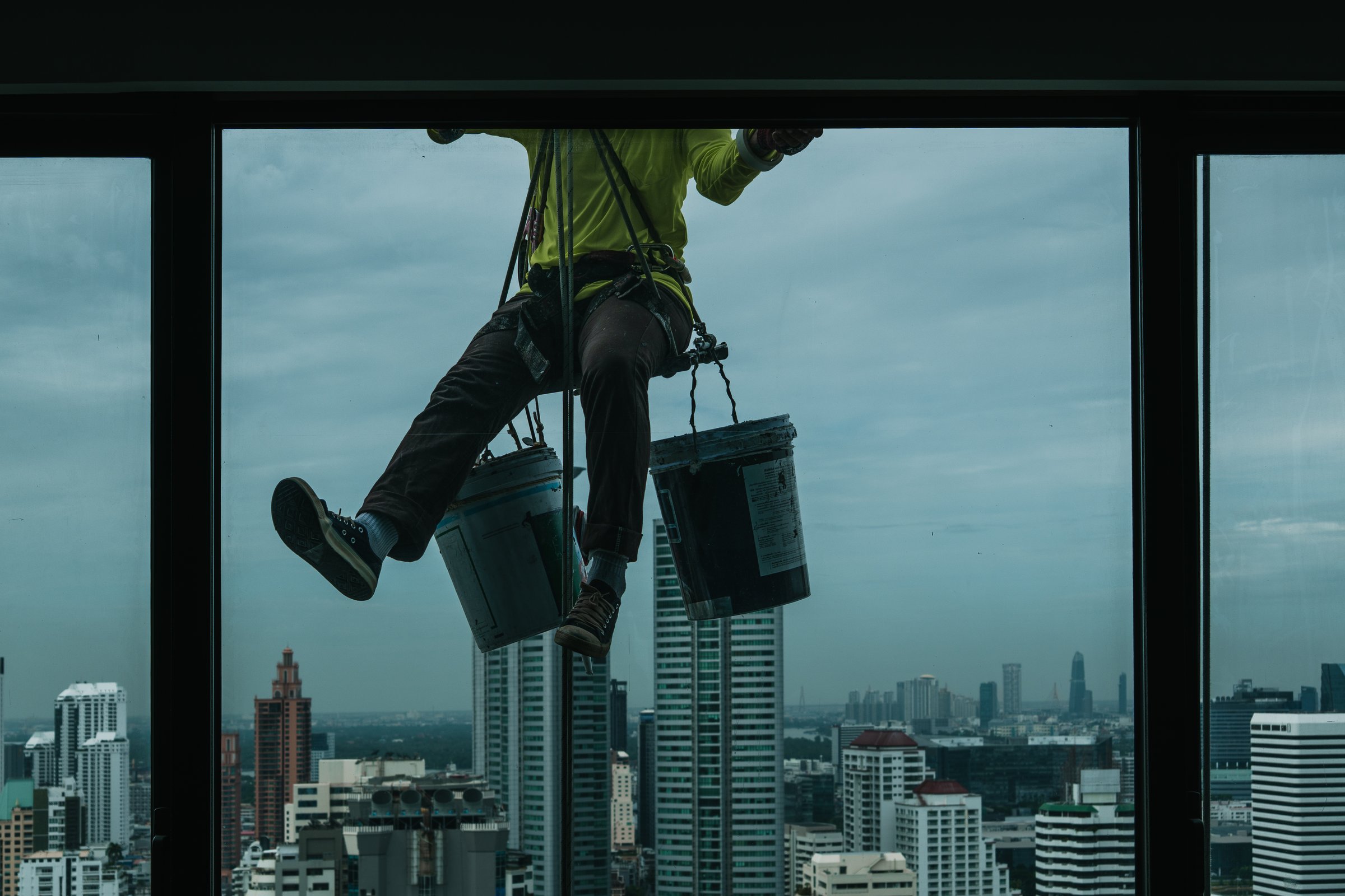 Window cleaner hanging with ropes and buckets cleaning the facade of a modern skyscraper in a big city