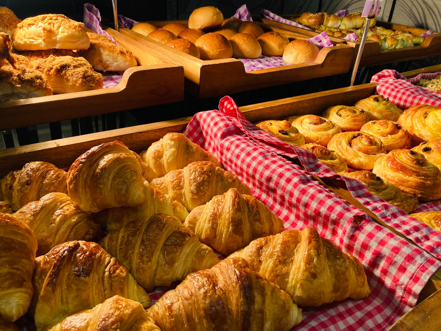 Freshly baked croissants and golden bread rolls on wooden display trays