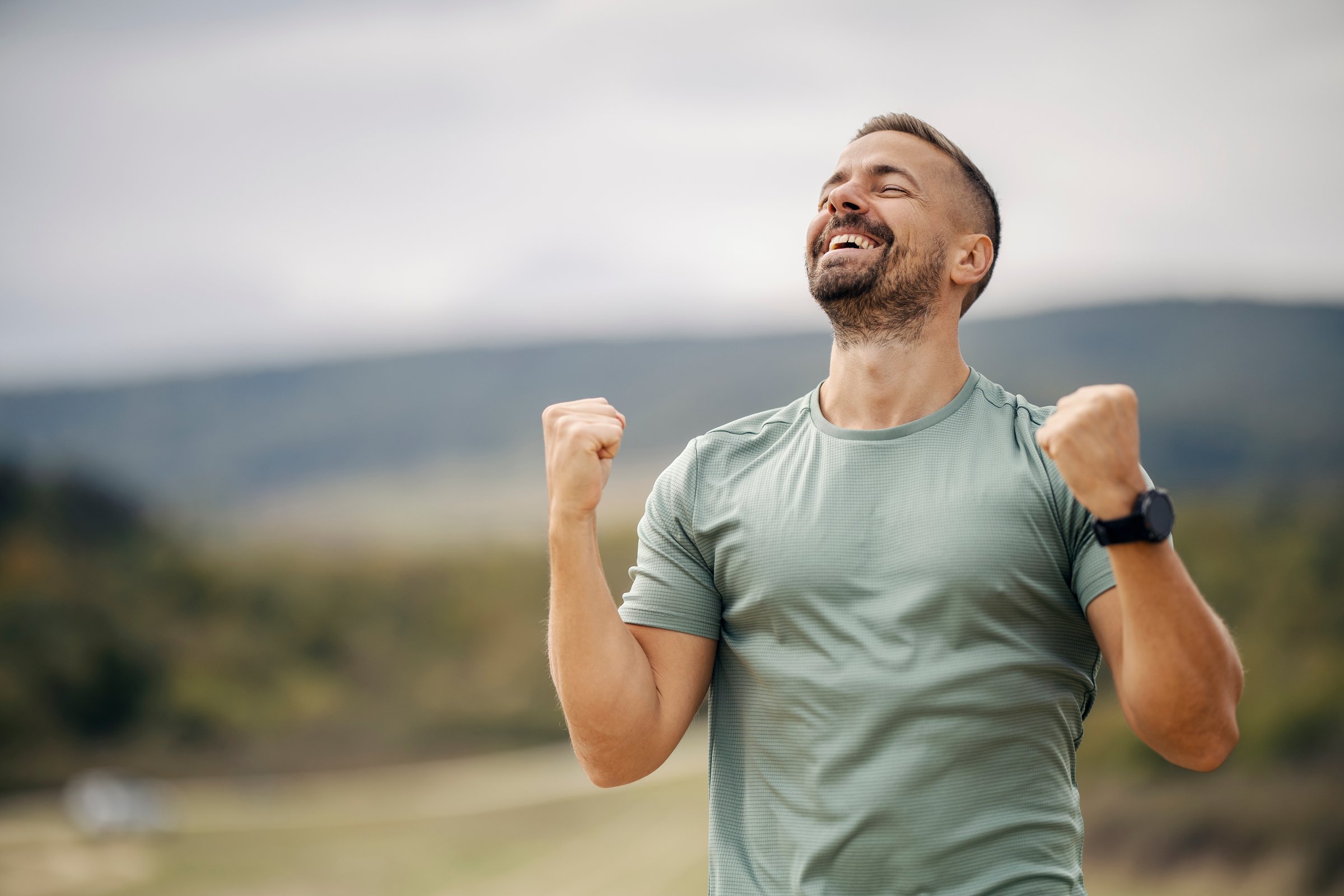 Man feeling happy and excited, celebrating achievement, raising fists in a victorious gesture after working out outdoors