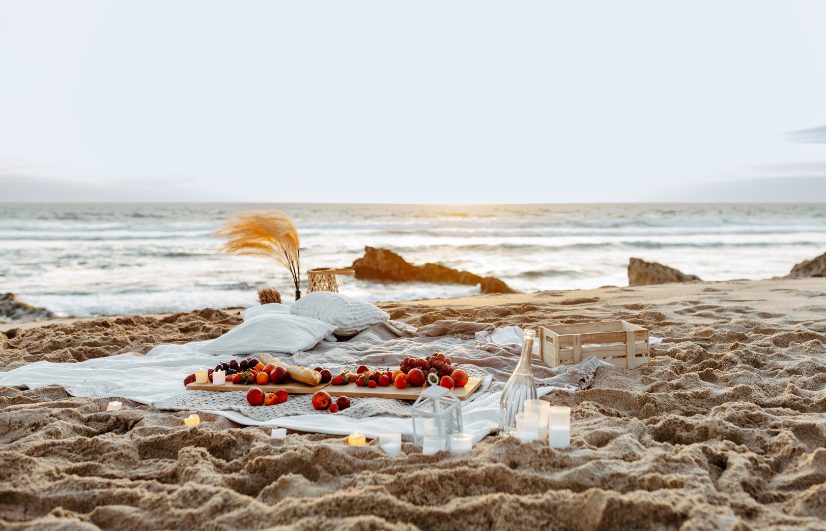 Having picnic with fresh fruits and rose wine on blanket at sandy beach over sea shore at background