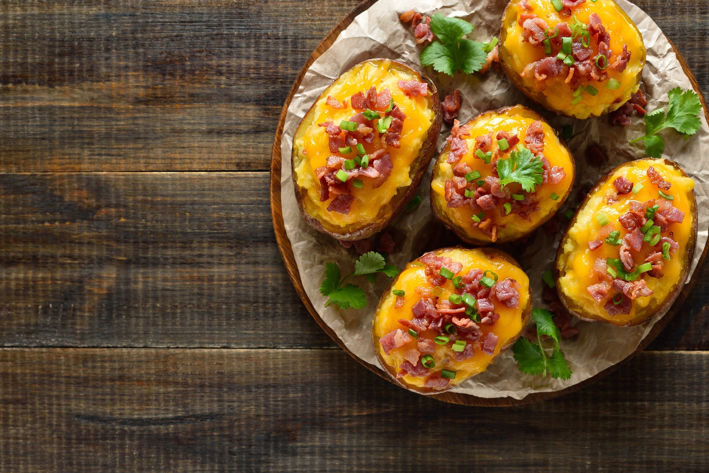 Baked stuffed potatoes with bacon, green onion and cheddar cheese over wooden background. Top view, flat lay