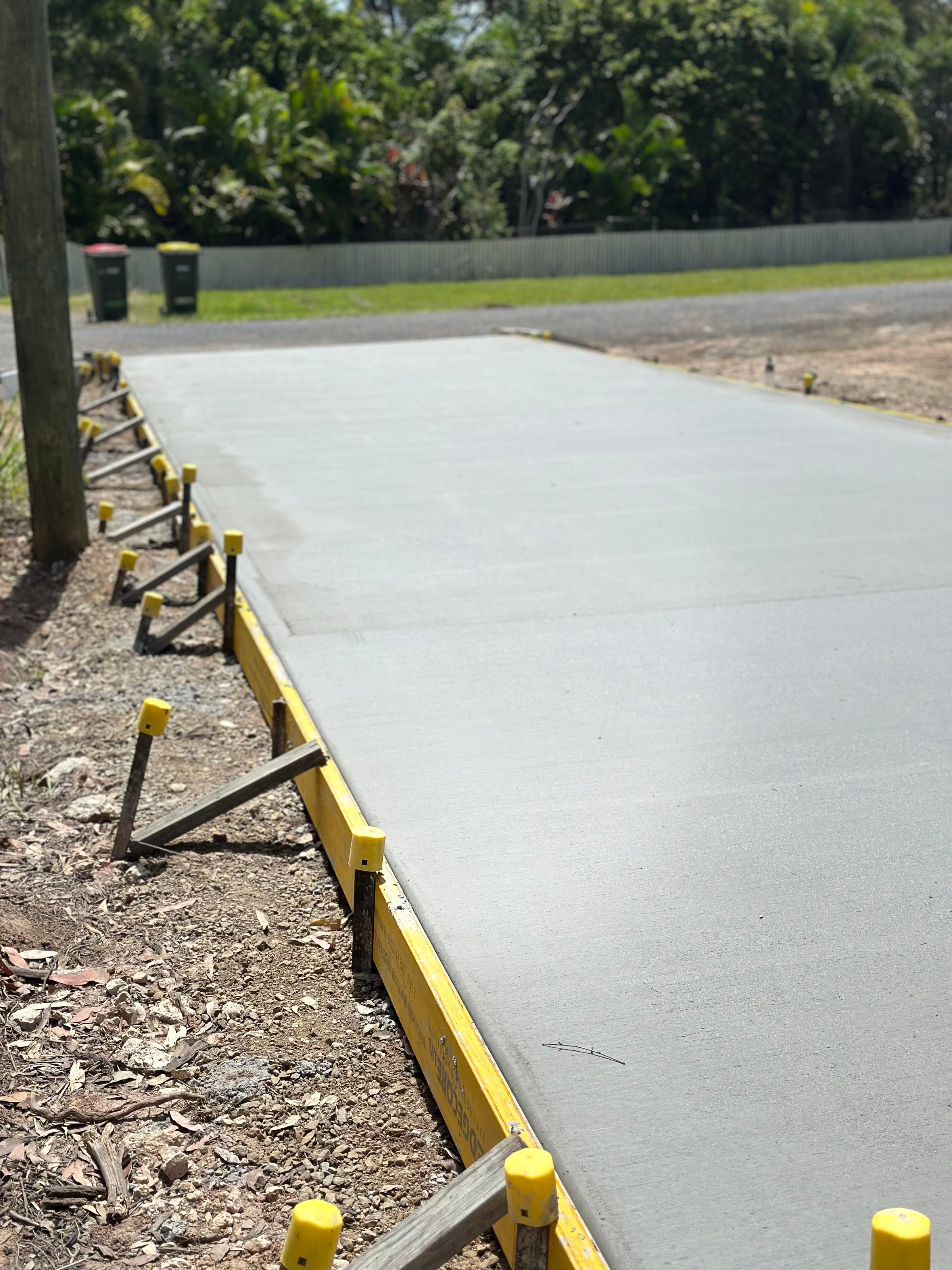 Freshly poured concrete slab supported by yellow formwork in an outdoor setting with trees in the background.