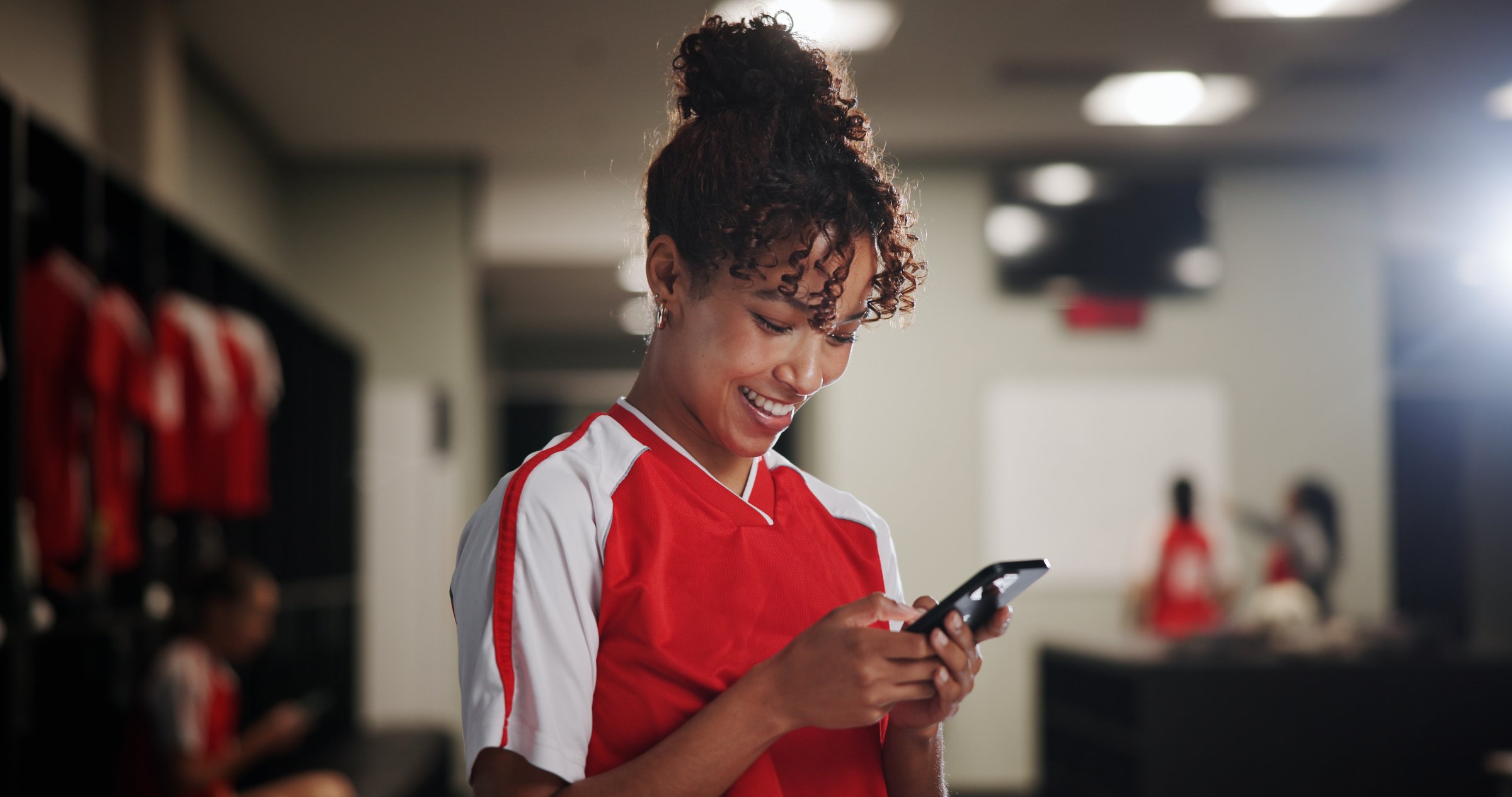 Sport, girl and smile in locker room with mobile, social media and check training schedule. Football player, woman and happy with phone for good news, league acceptance or favorite soccer team update