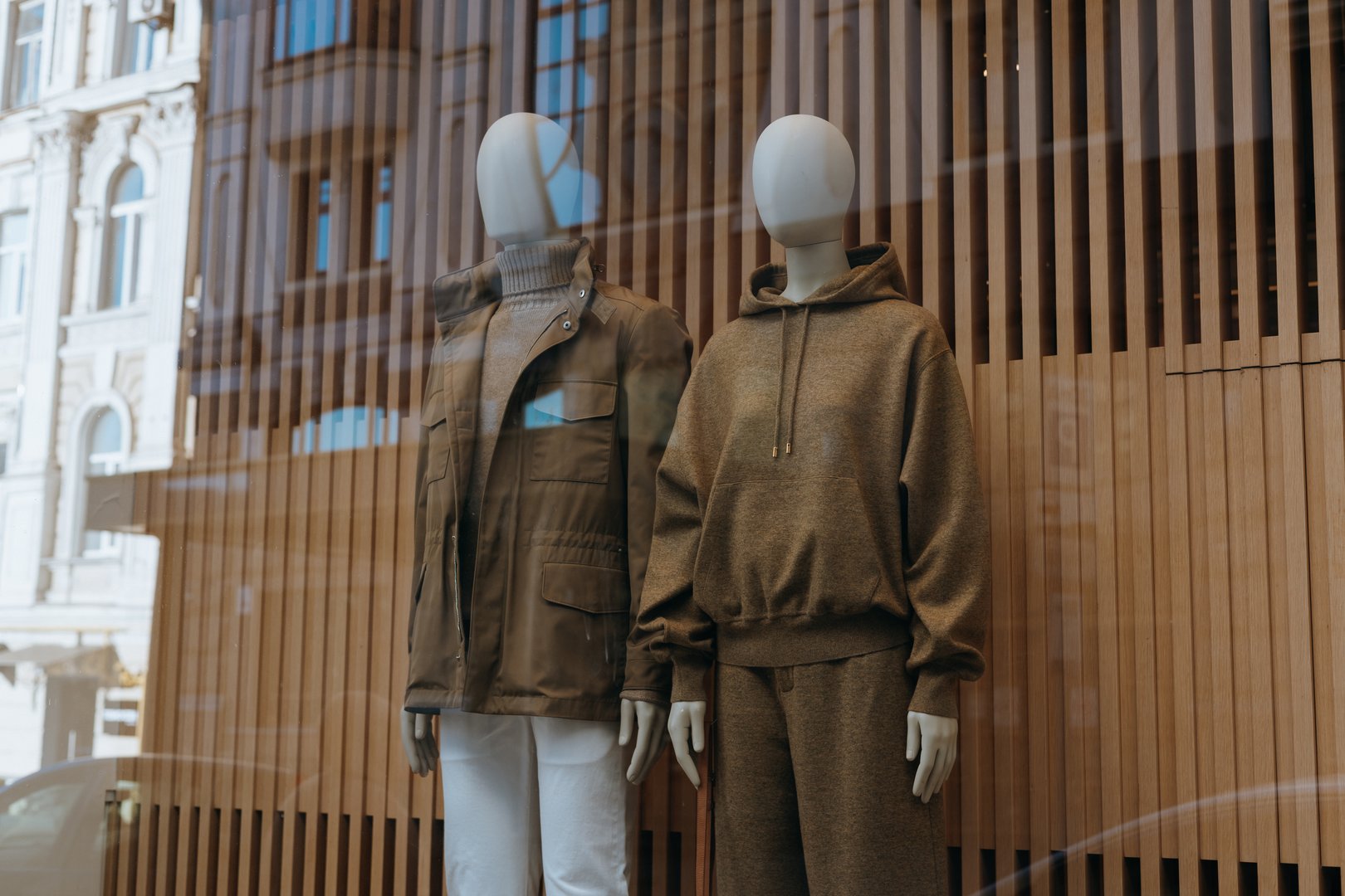 Fashionable window display Two mannequins in trendy casual fall, winter outfits featuring neutral colors, field jacket, a cozy hoodie, showcasing modern apparel trends.