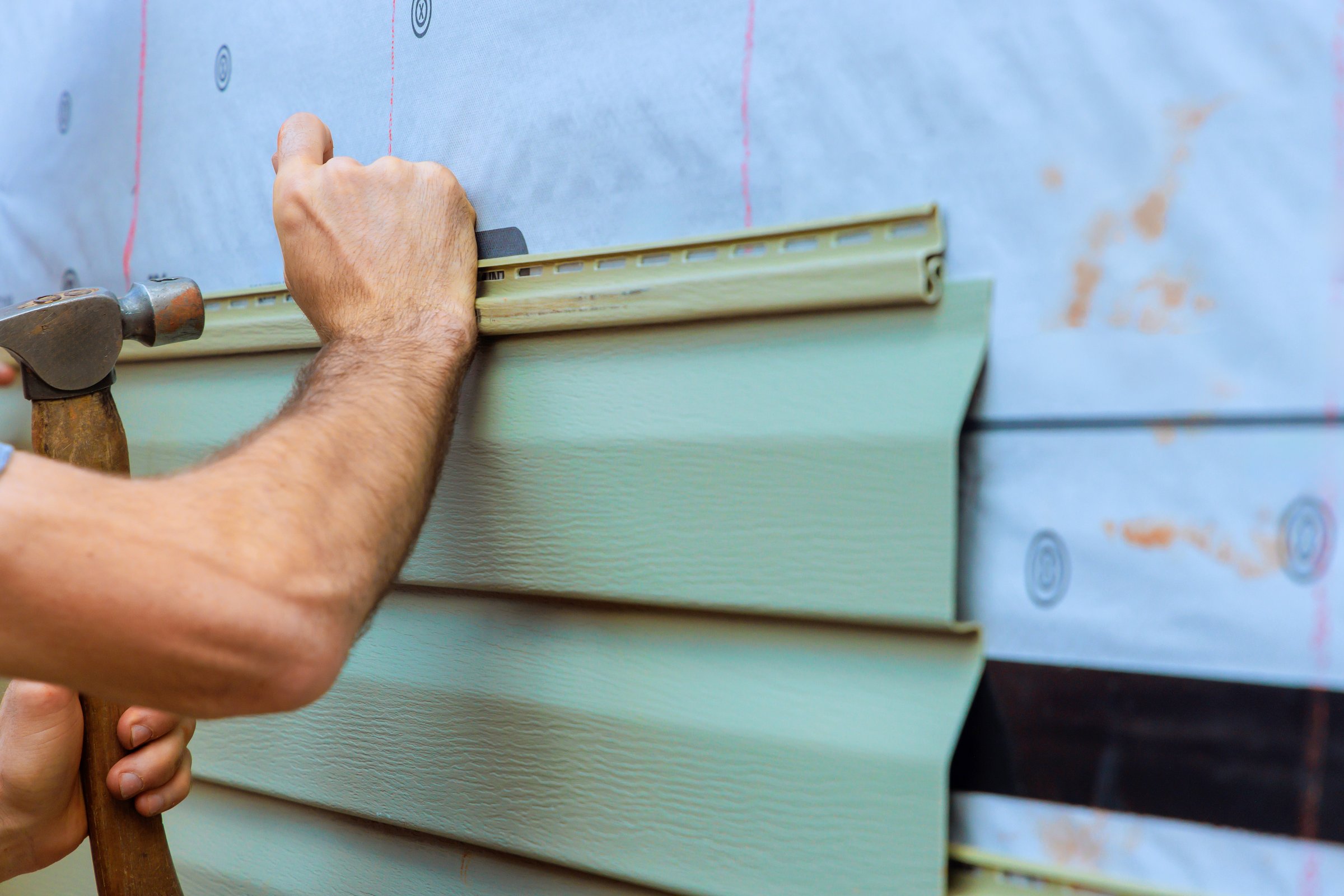 Contractor worker carefully attaches facade PVC siding to house, on precision craftsmanship in residential area.