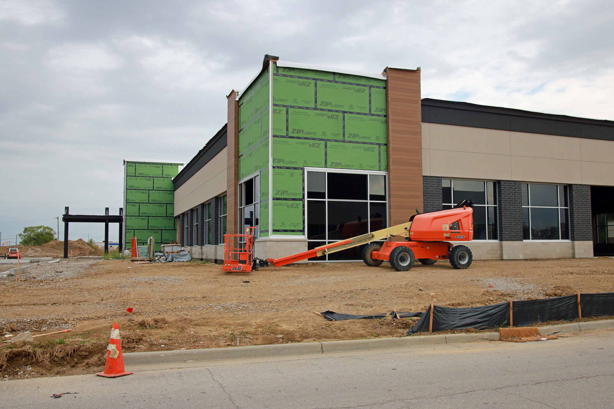 Greenwood, Indiana, USA -September 22 2024: A commercial real estate building under construction, featuring partially installed stone veneer and windows, with an unfinished parking lot and sidewalks.