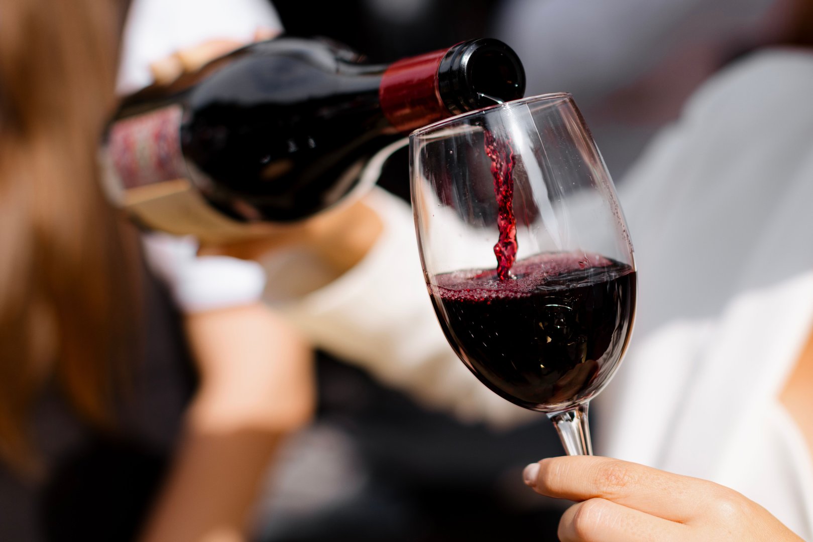 A Close-up of a person pouring red wine into a glass at an outdoor event, showcasing the wine's elegance and clarity