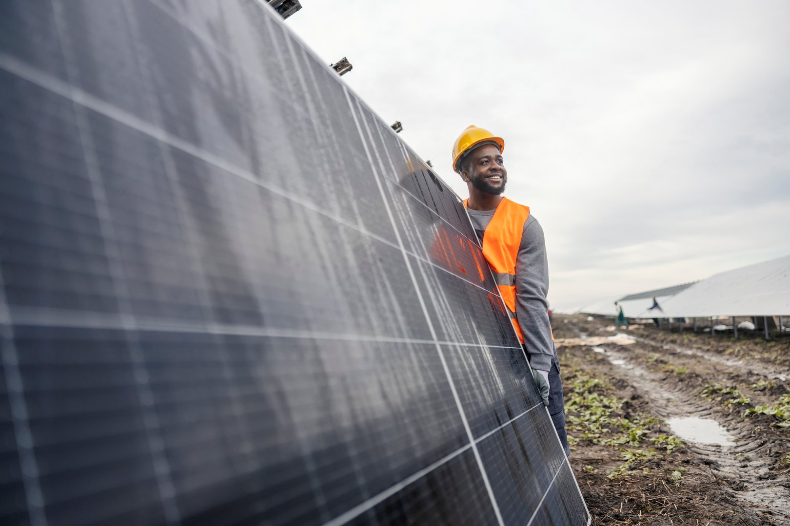 Happy multicultural worker carrying solar panel and preparing it for installation at solar farm.