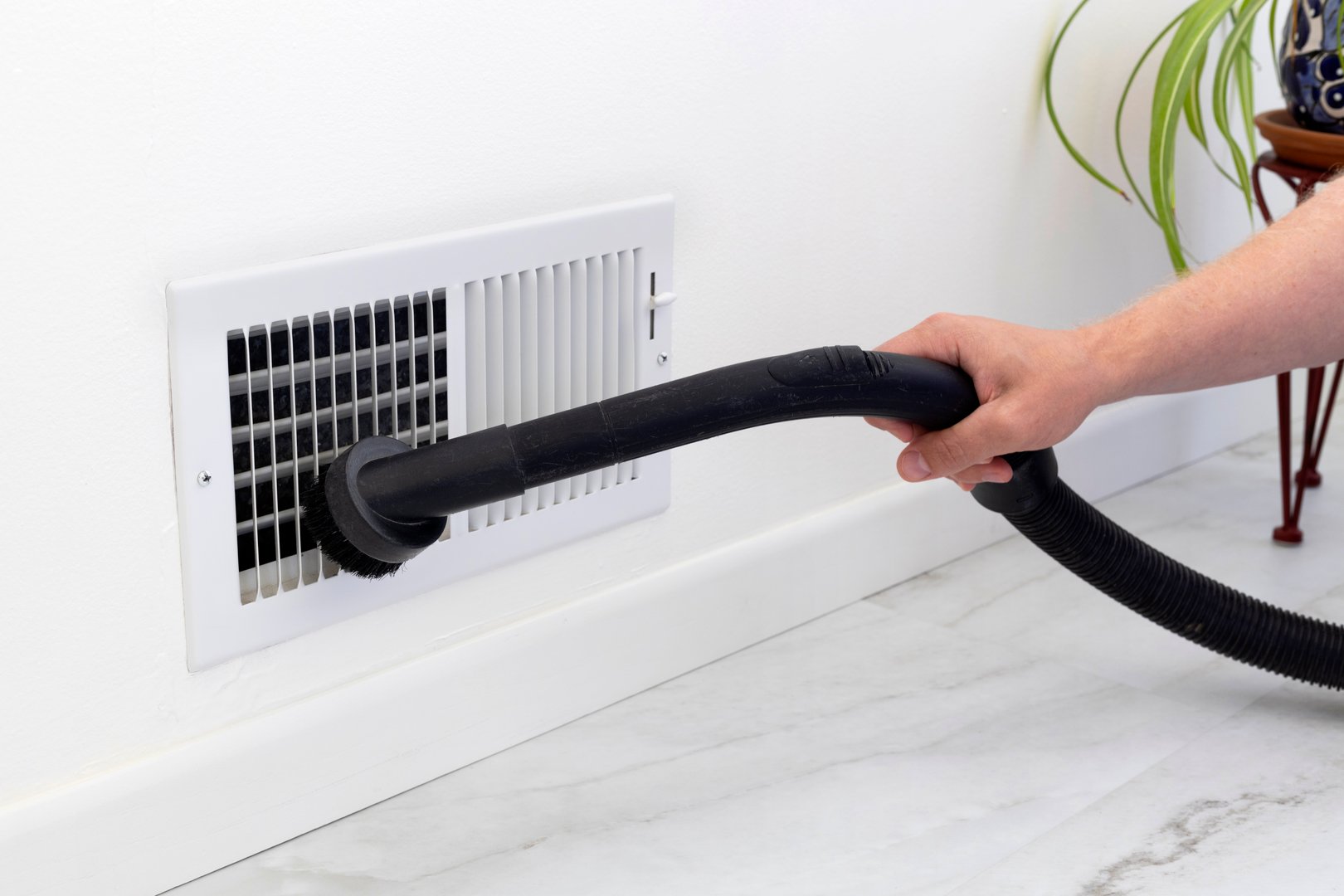 A person using a vacuum to clean the air vent cover
