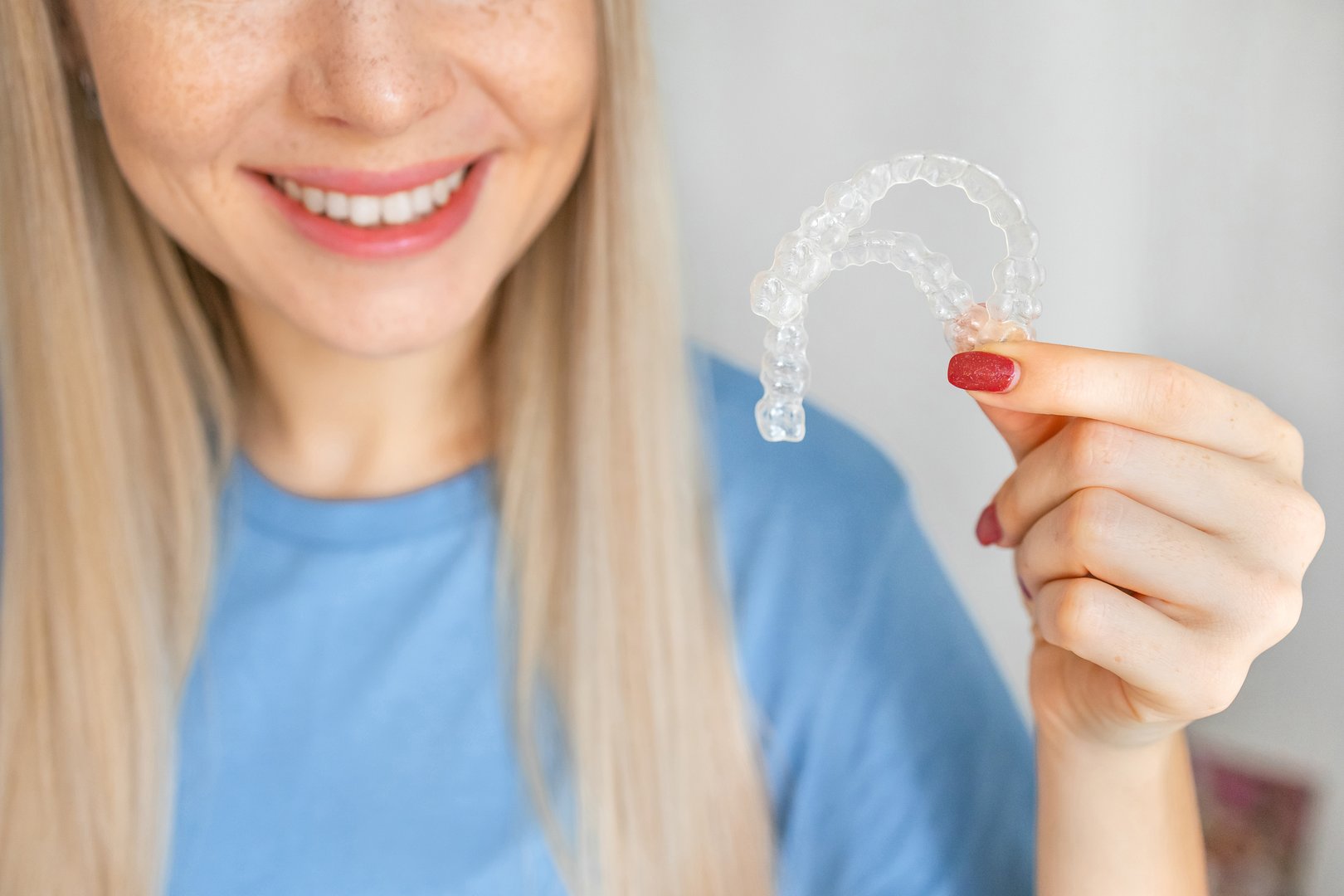 A smiling woman holding invisalign or invisible braces, orthodontic equipment