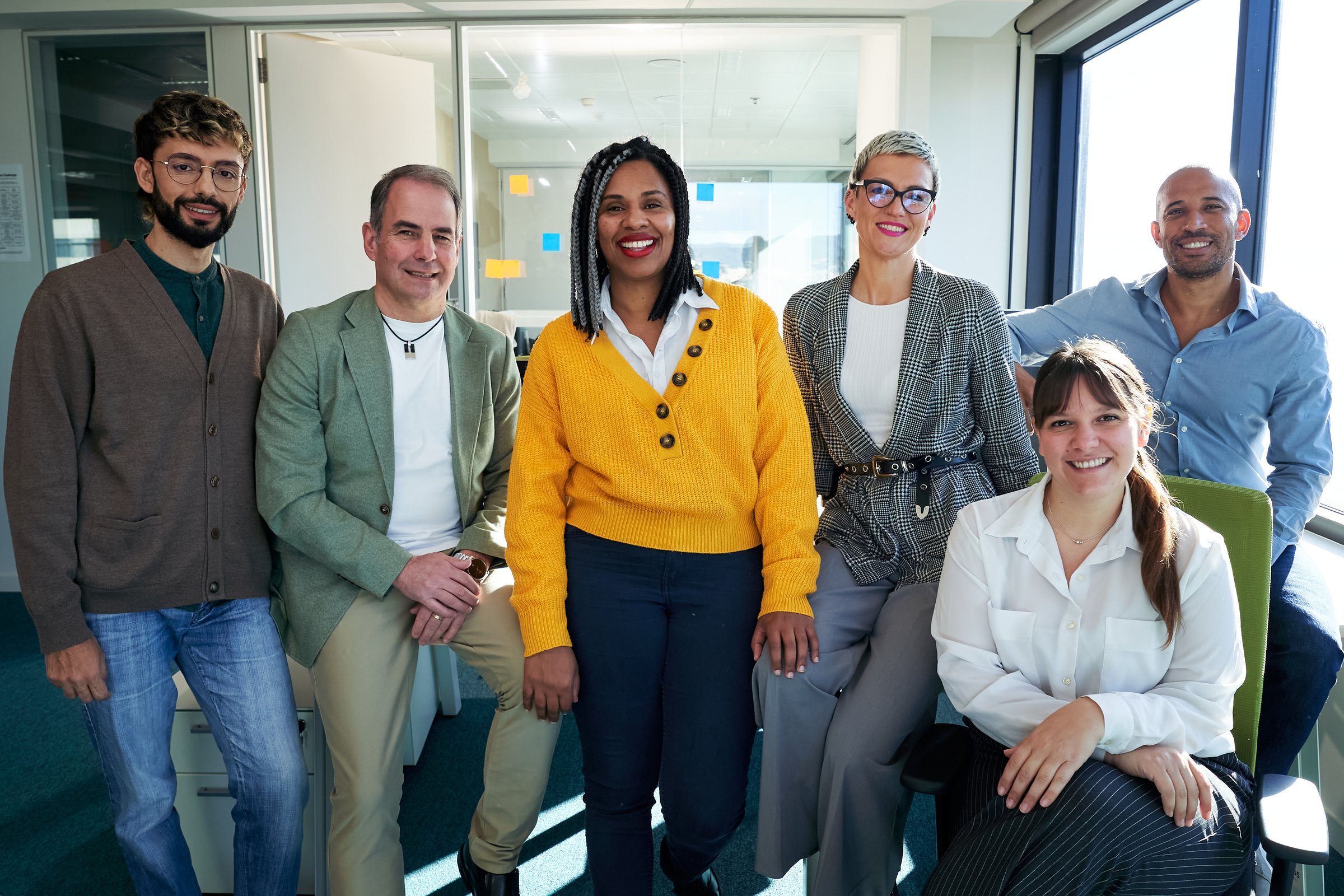 Portrait of a diverse team of professionals smiling together in a modern office, showing teamwork and collaboration, looking at camera cheerfully.