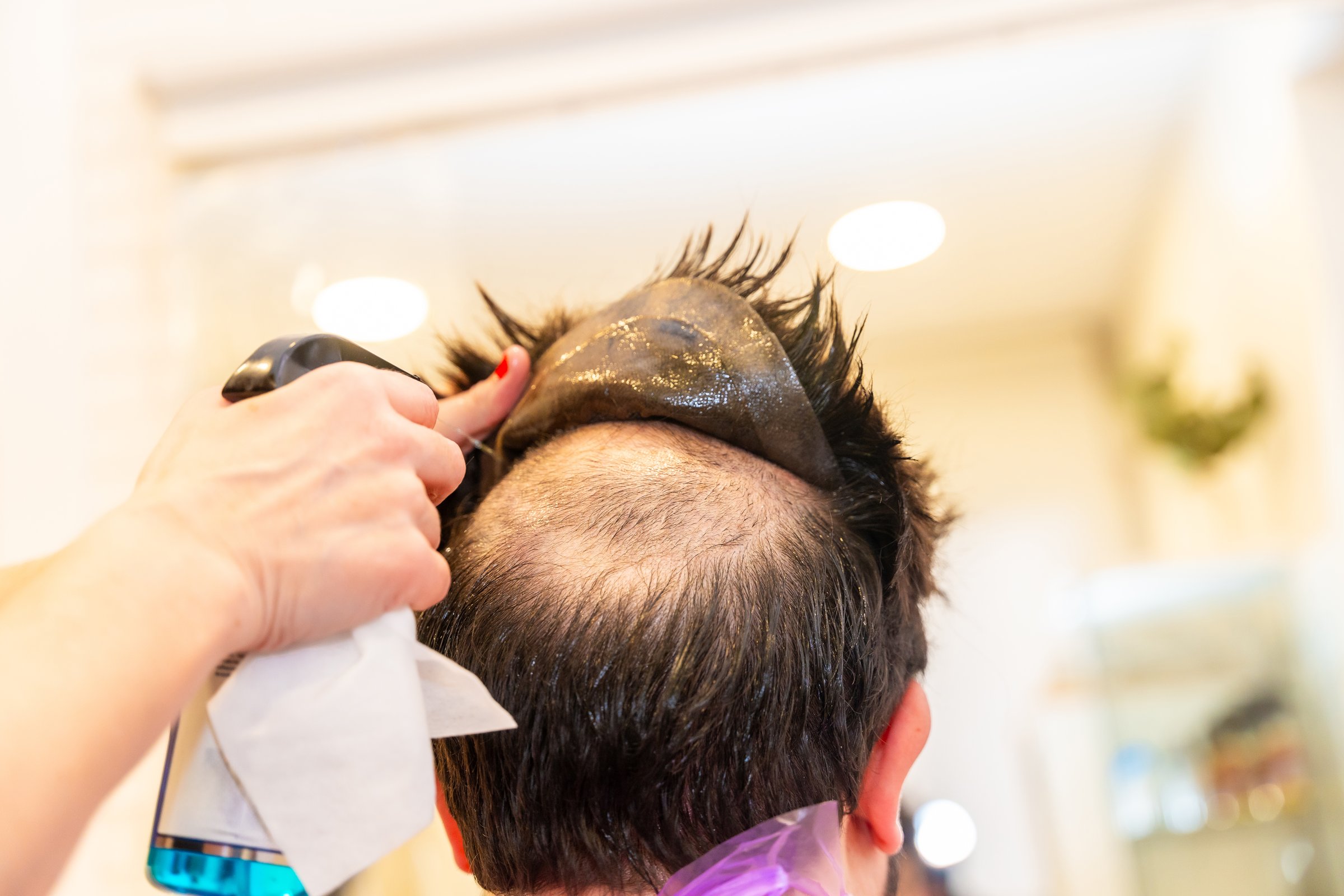 Rear view close-up of a Hairdresser removing the capillary prosthesis of a client using water spray