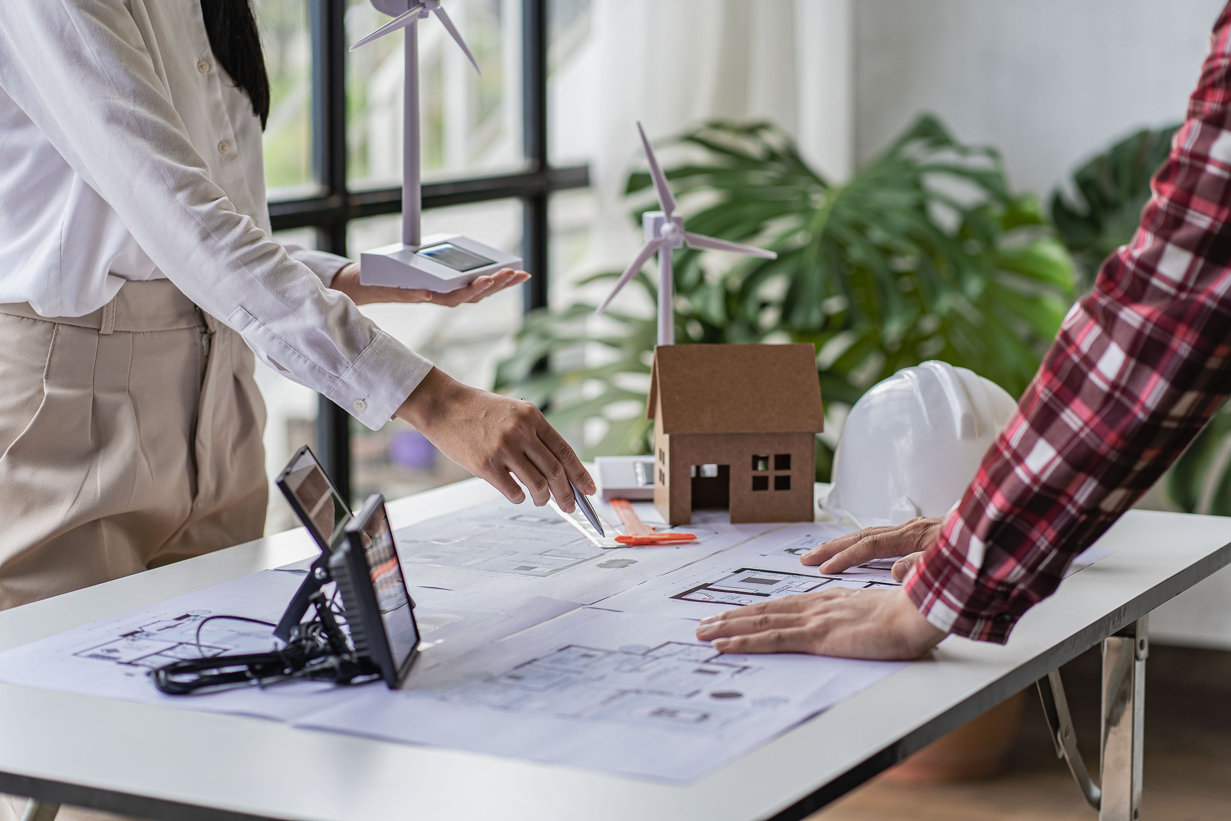 Engineers and residents are working on a house design for a construction project with wind turbines and solar cells with electric installation, energy saving ideas.