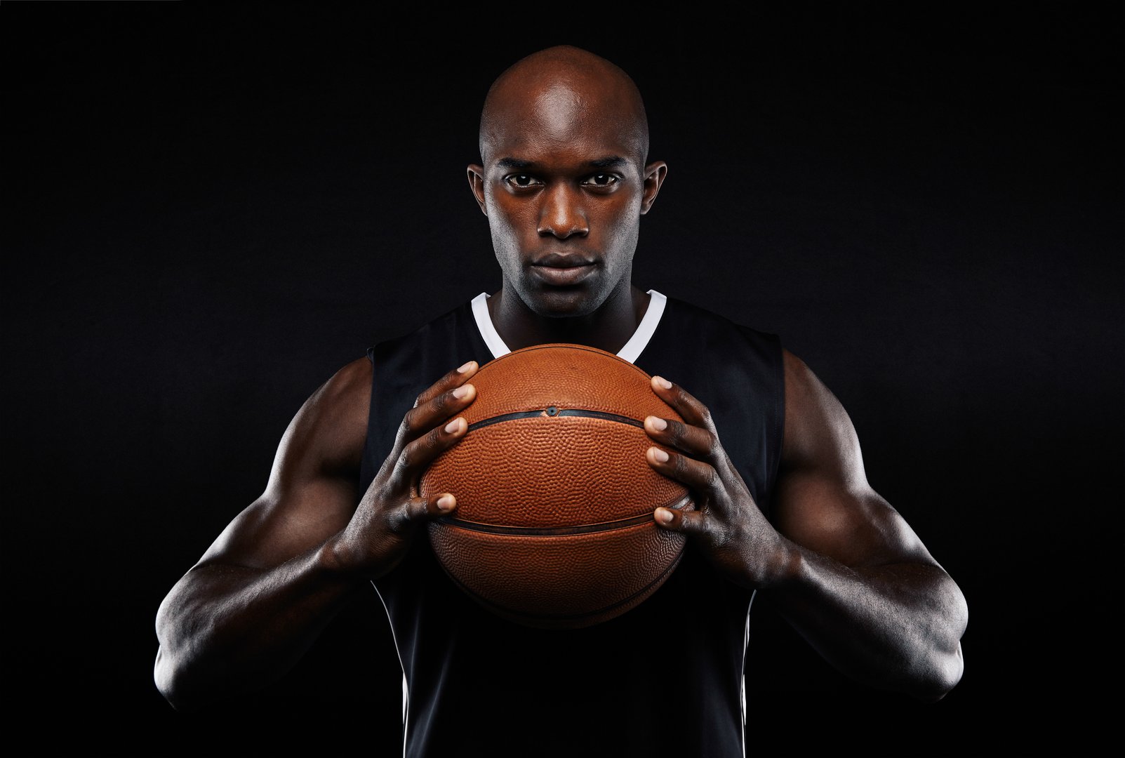 Portrait of afro american male basketball player with a ball over black background. Fit young man in sportswear holding basketball.