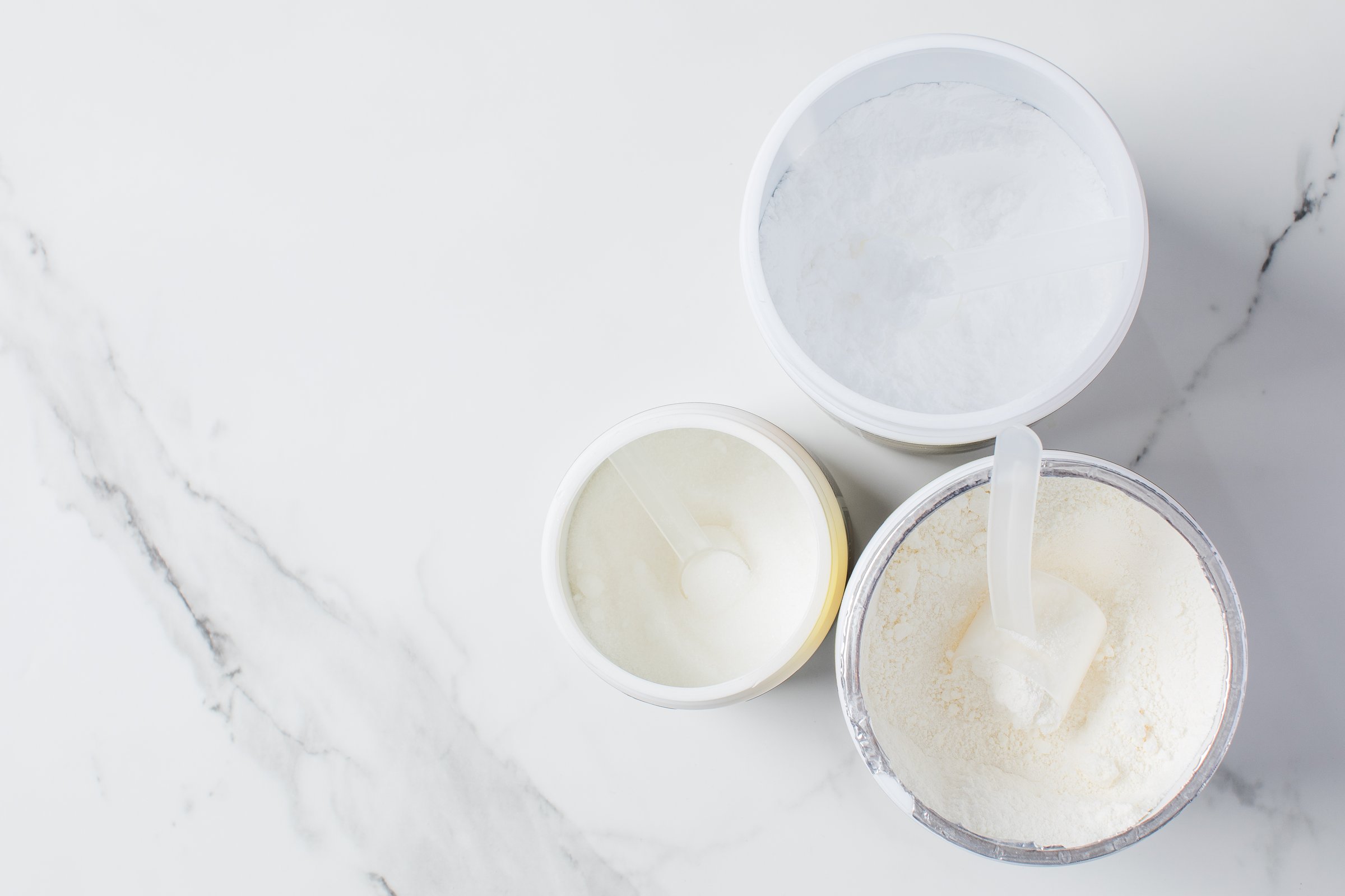 Assorted protein powder and supplement scoops on white marble background for nutrition and fitness. Copy space