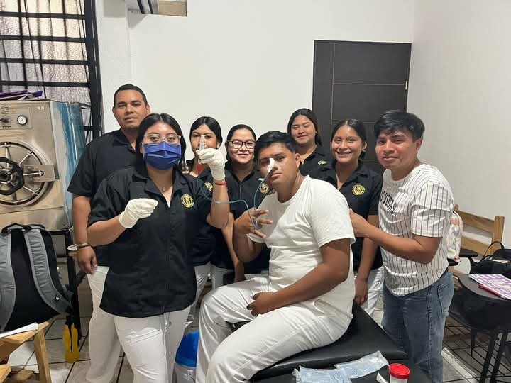 Group of nursing students practicing a medical procedure with a patient in a clinical room setting.