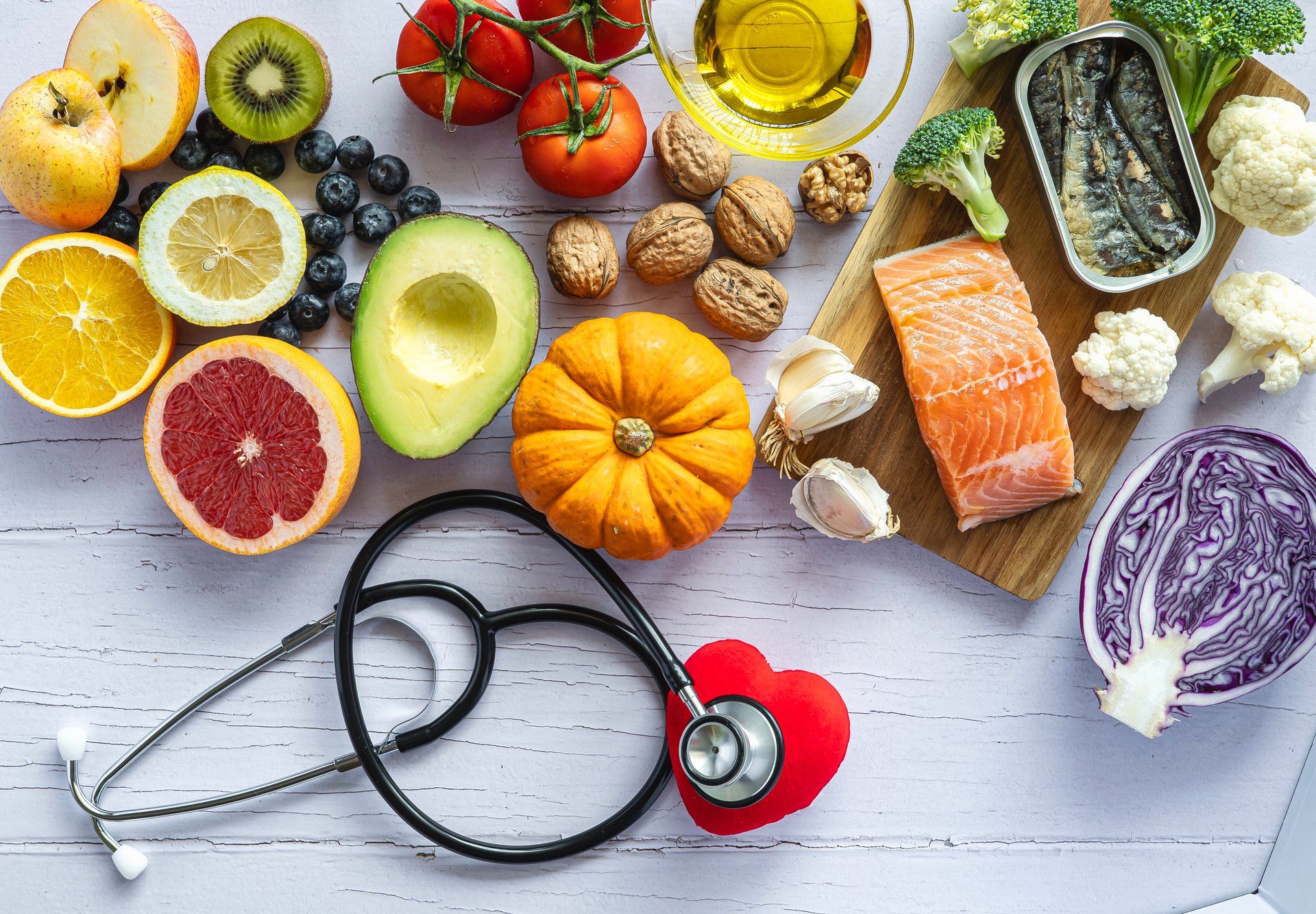 Stethoscope hiding a heart surrounded by healthy food: fruit, vegetables, fish. Healthy food concept to prevent diseases