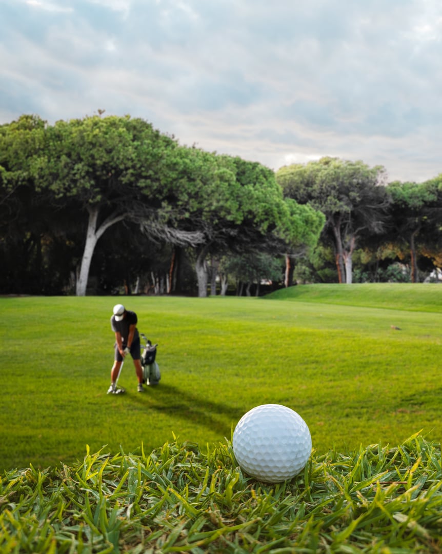 Golf ball on a golf green in the foreground and silhouette of a player at the background.