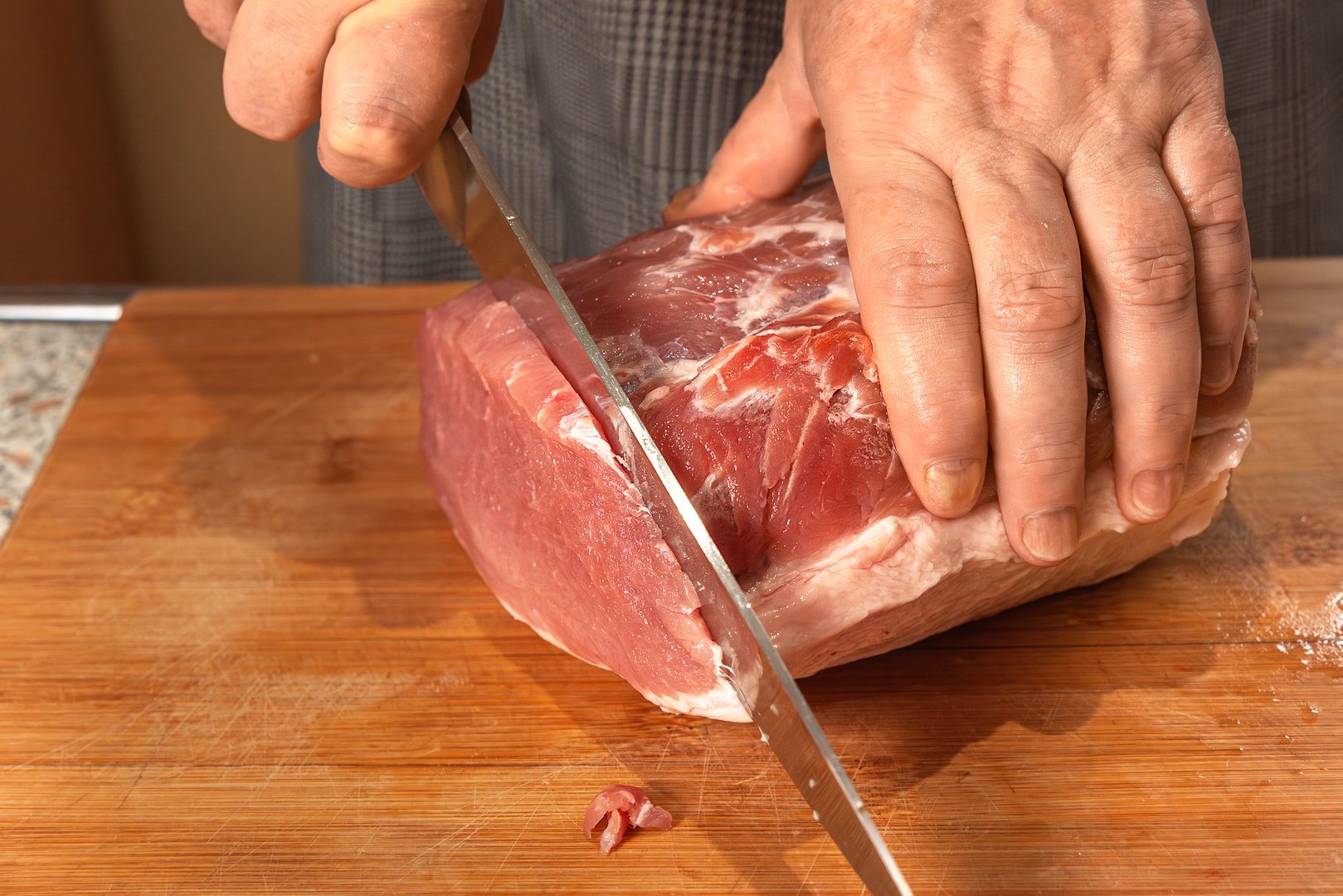 Cook cuts a piece of raw meat fillet into steaks or chops with a knife. Close-up