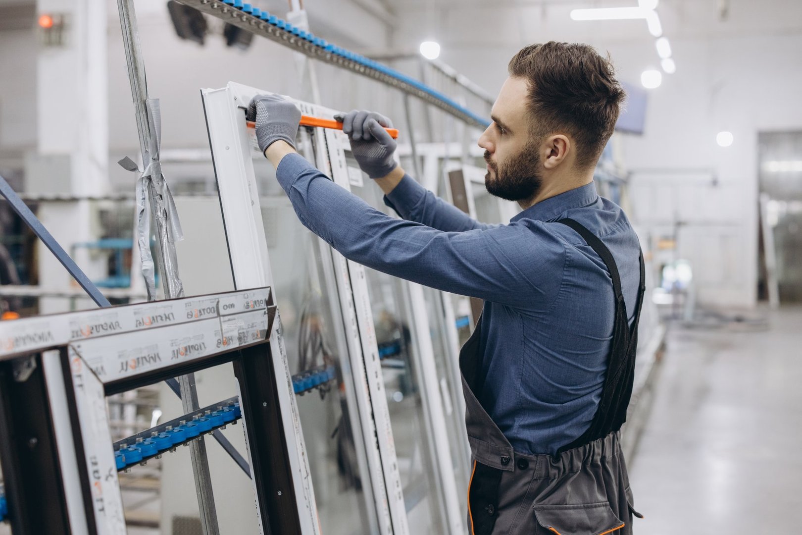 Factory worker wearing uniform and gloves using ruler to measure PVC window frame in production line of aluminum and PVC windows and doors factory
