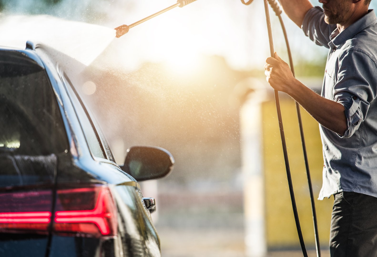 A Caucasian Car Wash Worker Cleaning Exterior Of Customers Car By Spraying Water And Rinsing Dirt