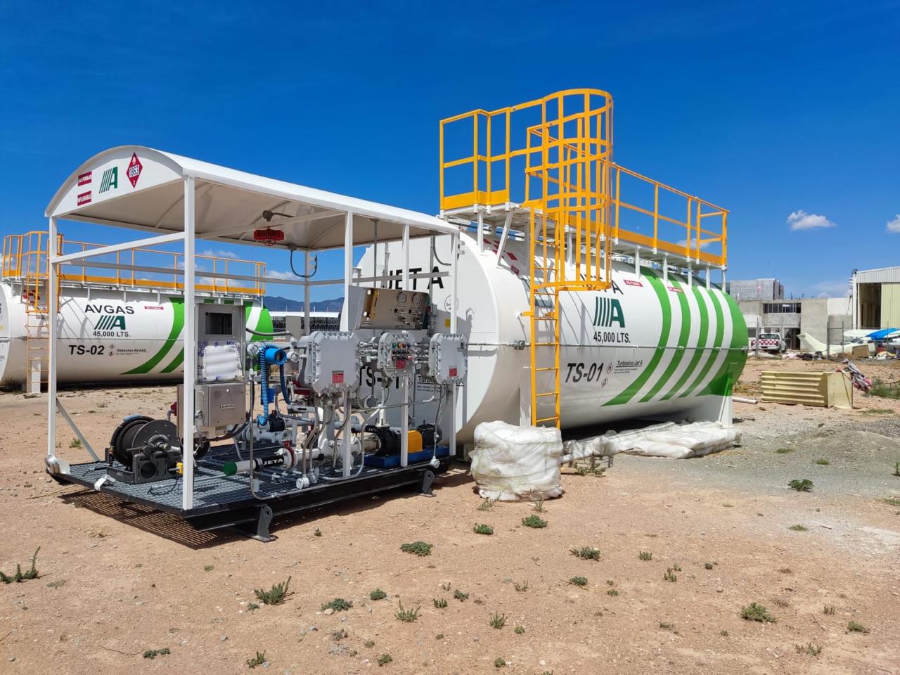 Fuel storage tanks with striped green paint, labeled TS-01 and TS-02, equipped with connected machinery on a gravel surface.