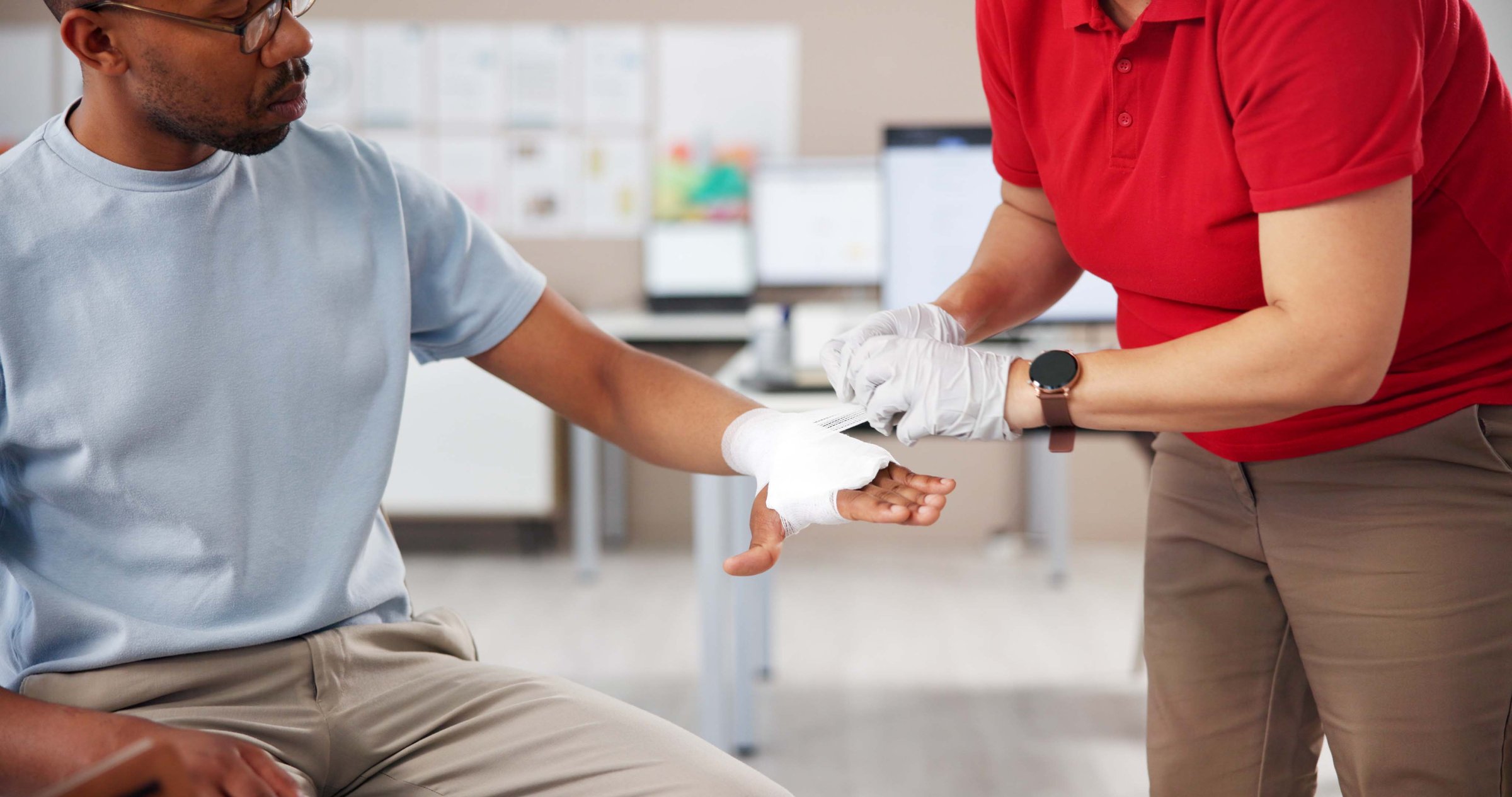 Hands, people and first aid with bandage, teaching or tutorial with care, attention or help at office. Paramedic, coach and staff for treatment, wound or burn injury with training course in workplace