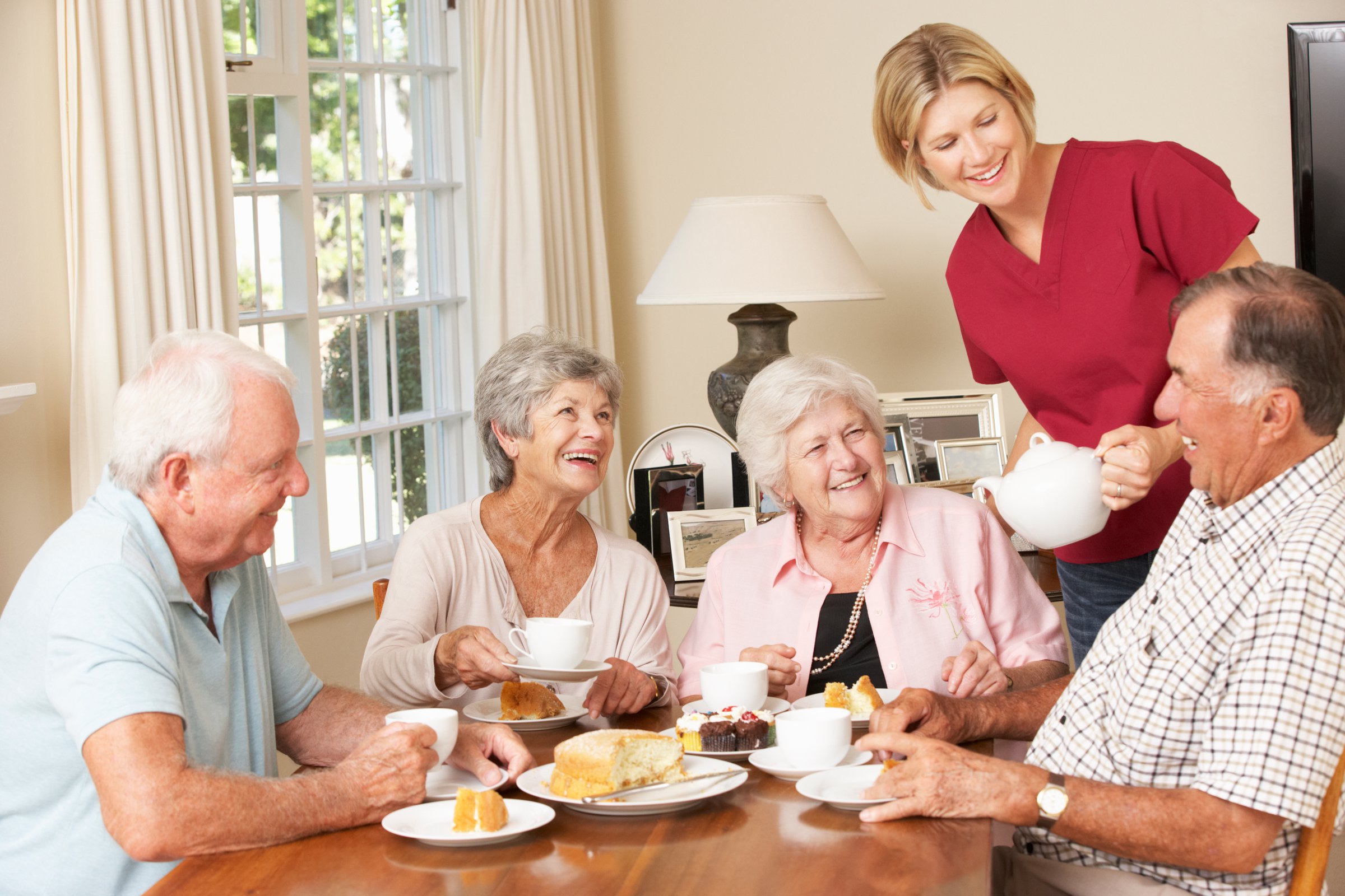 Group Of Senior Couples Enjoying Afternoon Tea Together At Home With Home Help. Having Fun