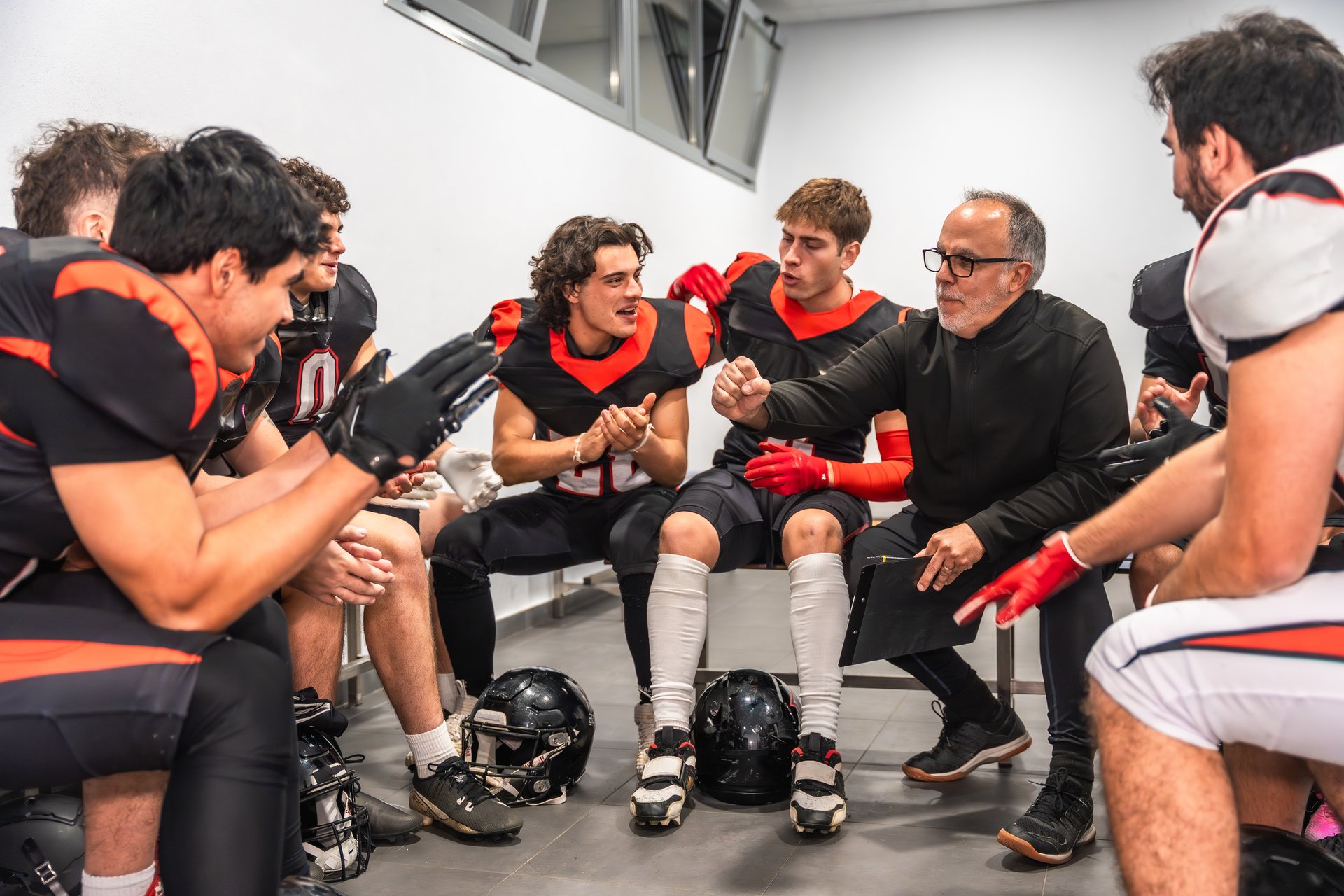 American football coach addresses his young adult team in the locker room, delivering a focused pep talk on strategy, teamwork and motivation before the game