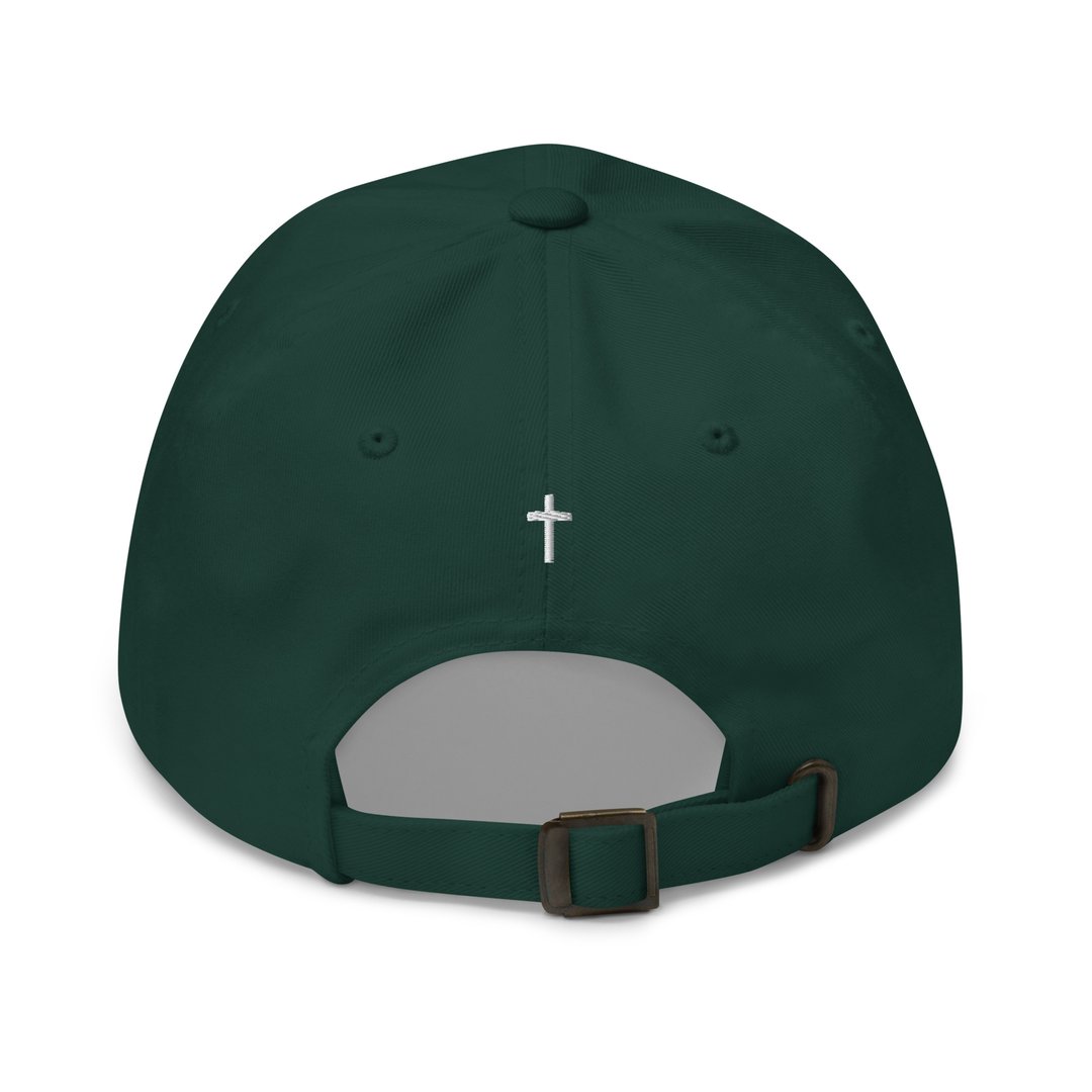 Green baseball cap with a small white cross embroidered on the back. Adjustable strap with metal buckle.