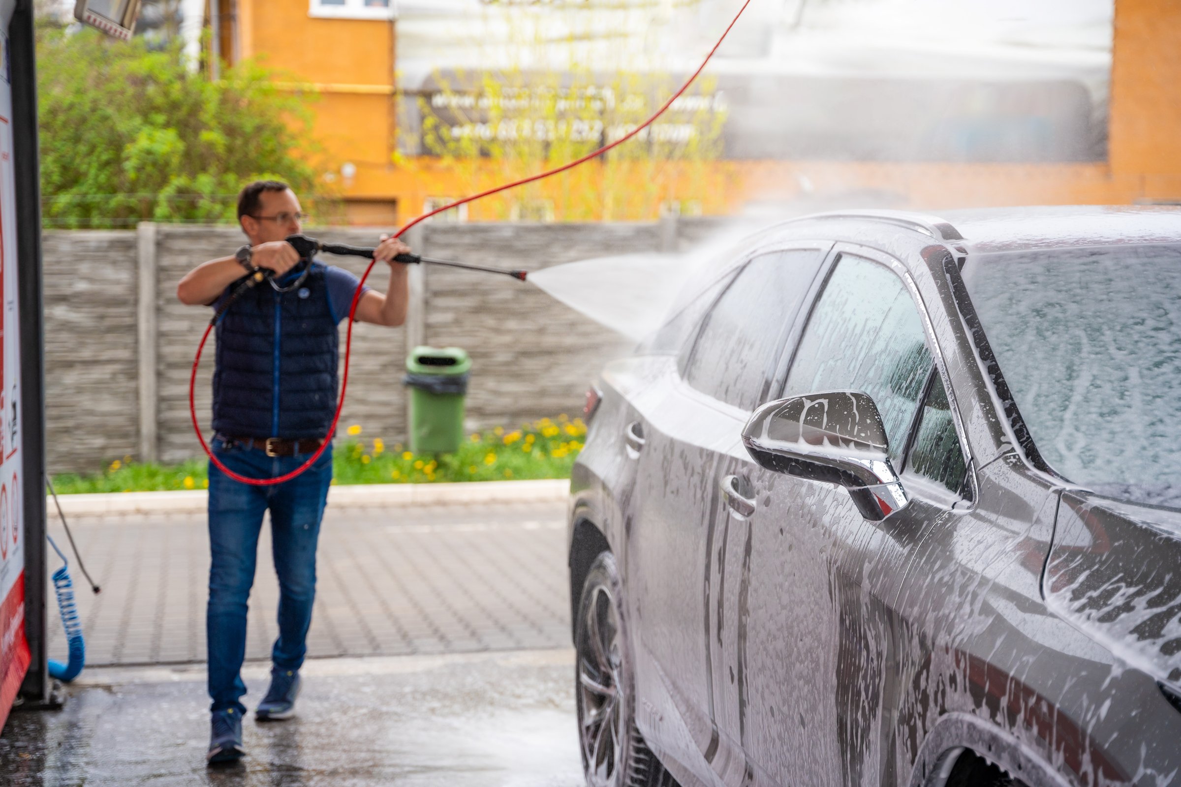Young man washes his car at a self-service car wash using a hose with pressurized water and foam. High quality photo